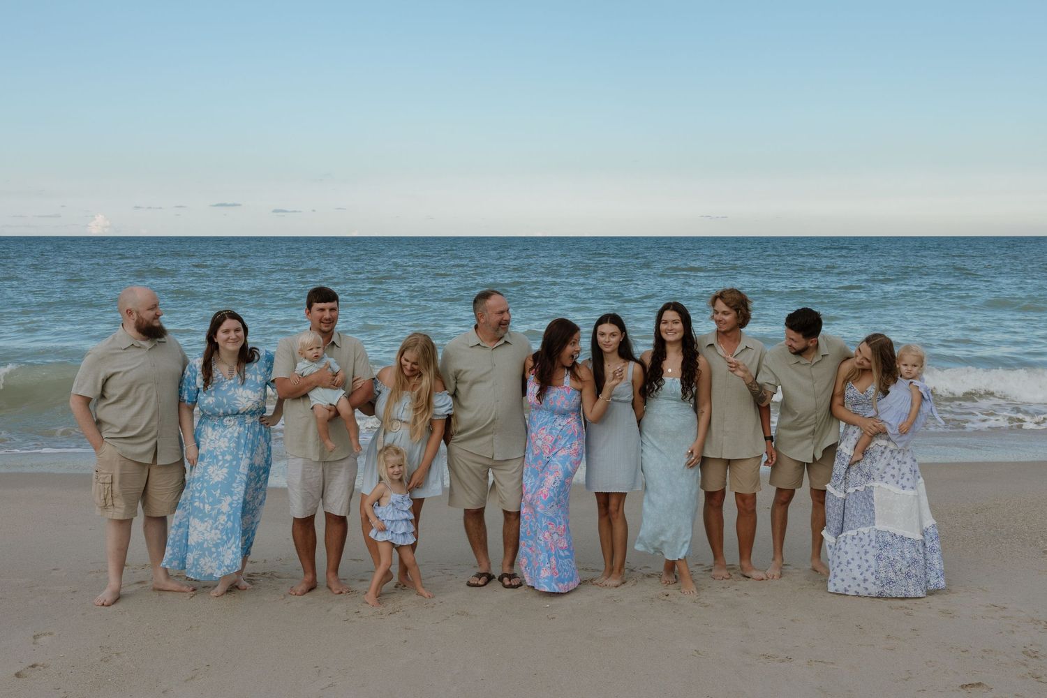 A group of people sitting together on a sandy beach at sunset with ocean waves in the background.