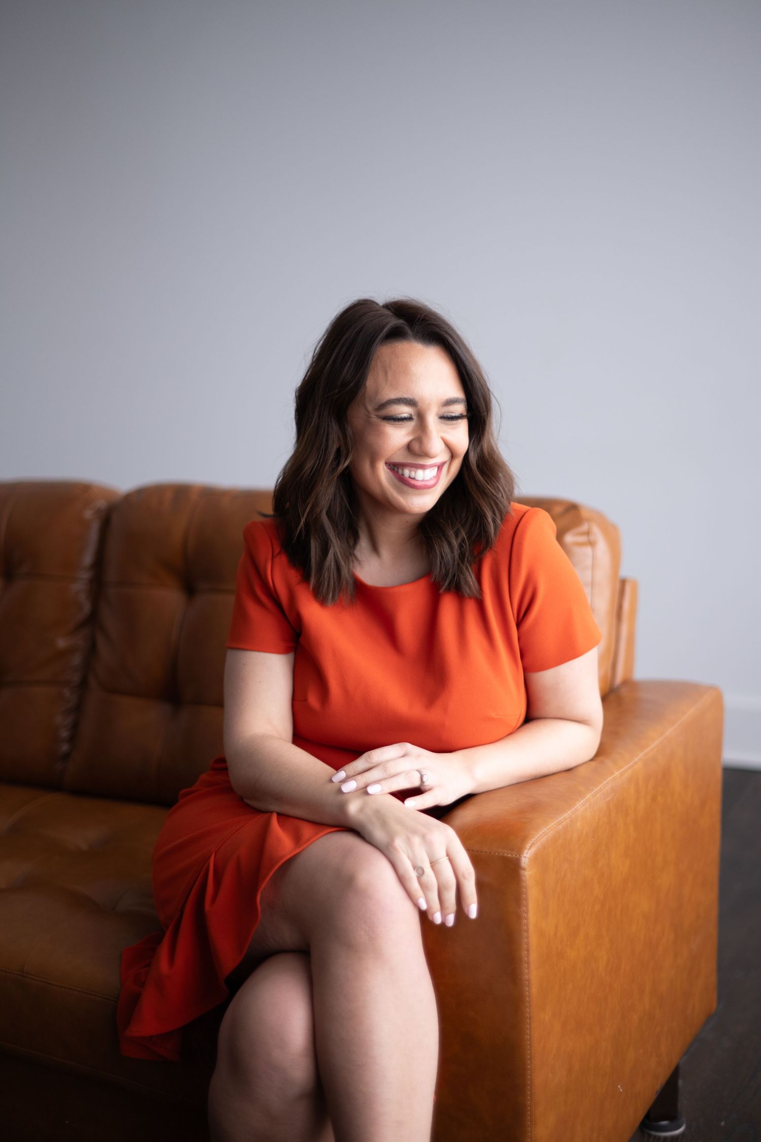 A series of candid shots showing someone in an orange dress sitting and laughing on a brown leather couch.