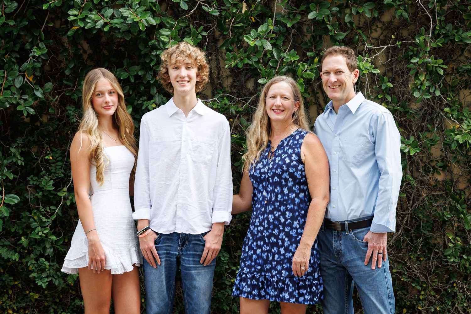 A family poses for a family portrait against a wall of ivy in Haile Plantation Village Center in Gainesville, Fl.