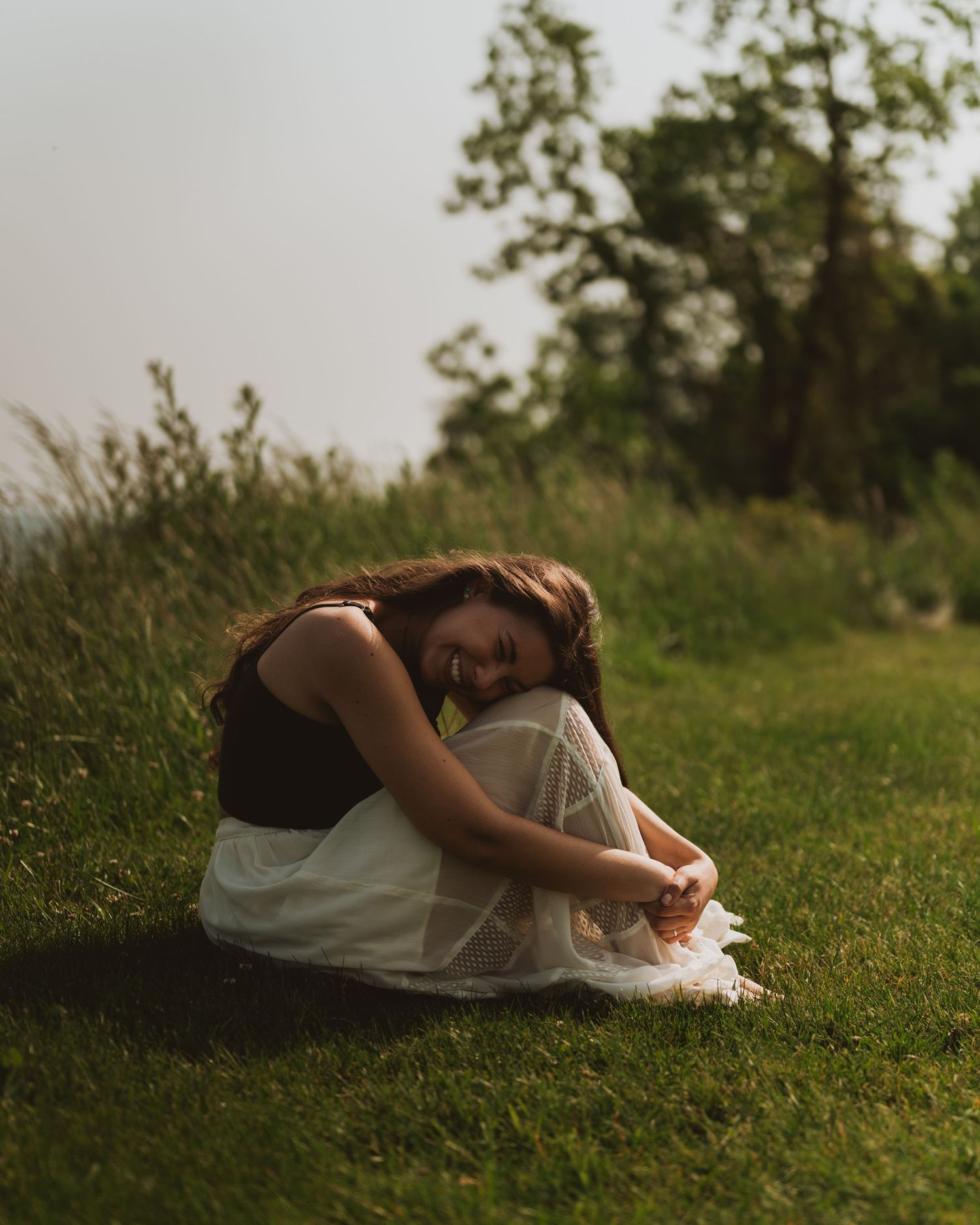 Person lying in curled up position on grassy hillside during golden sunset hour.