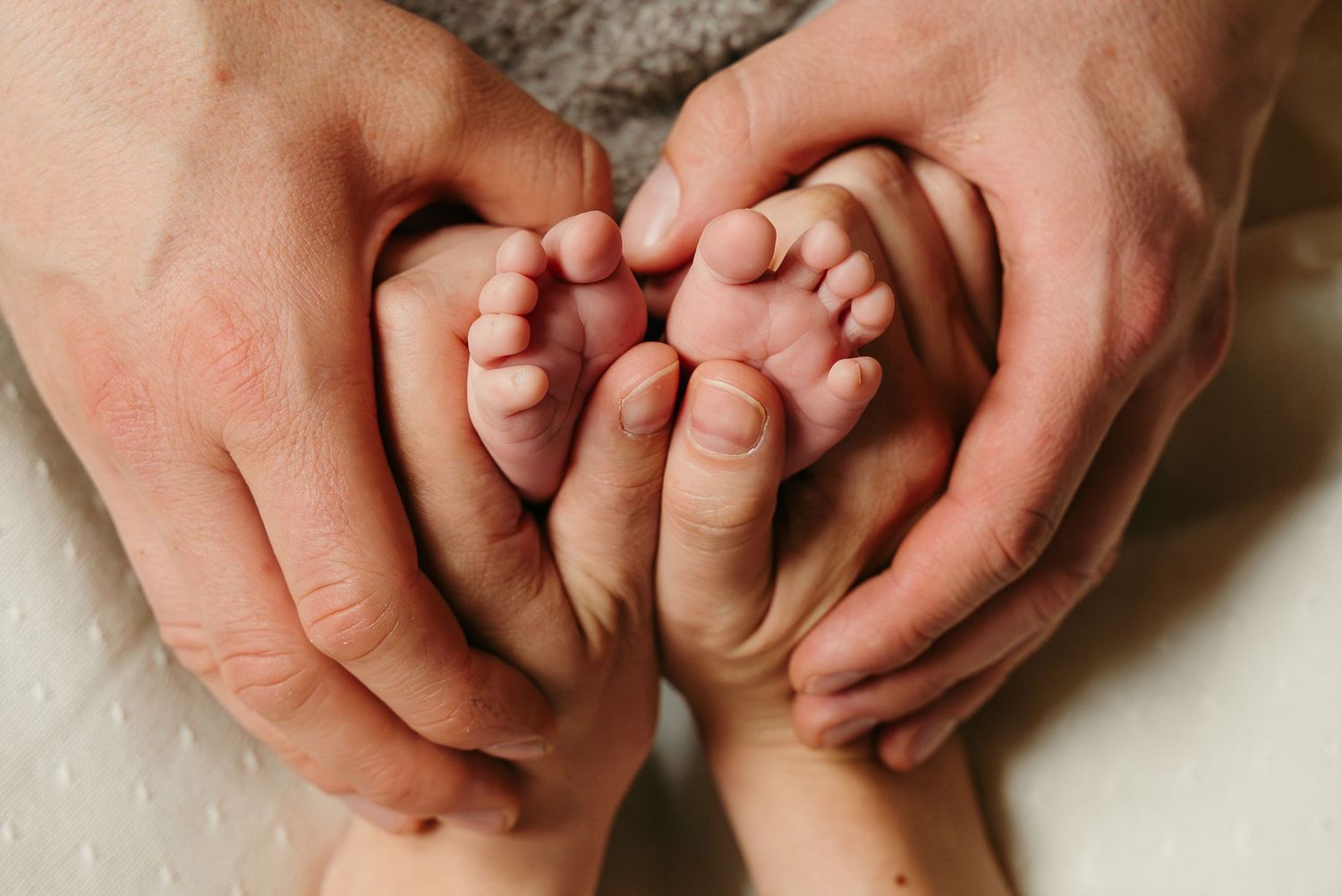 Maminka dává pusinku na hlavičku newborn narozeného miminka, které drží v náruči tatínek a všichni jsou spolu doma.