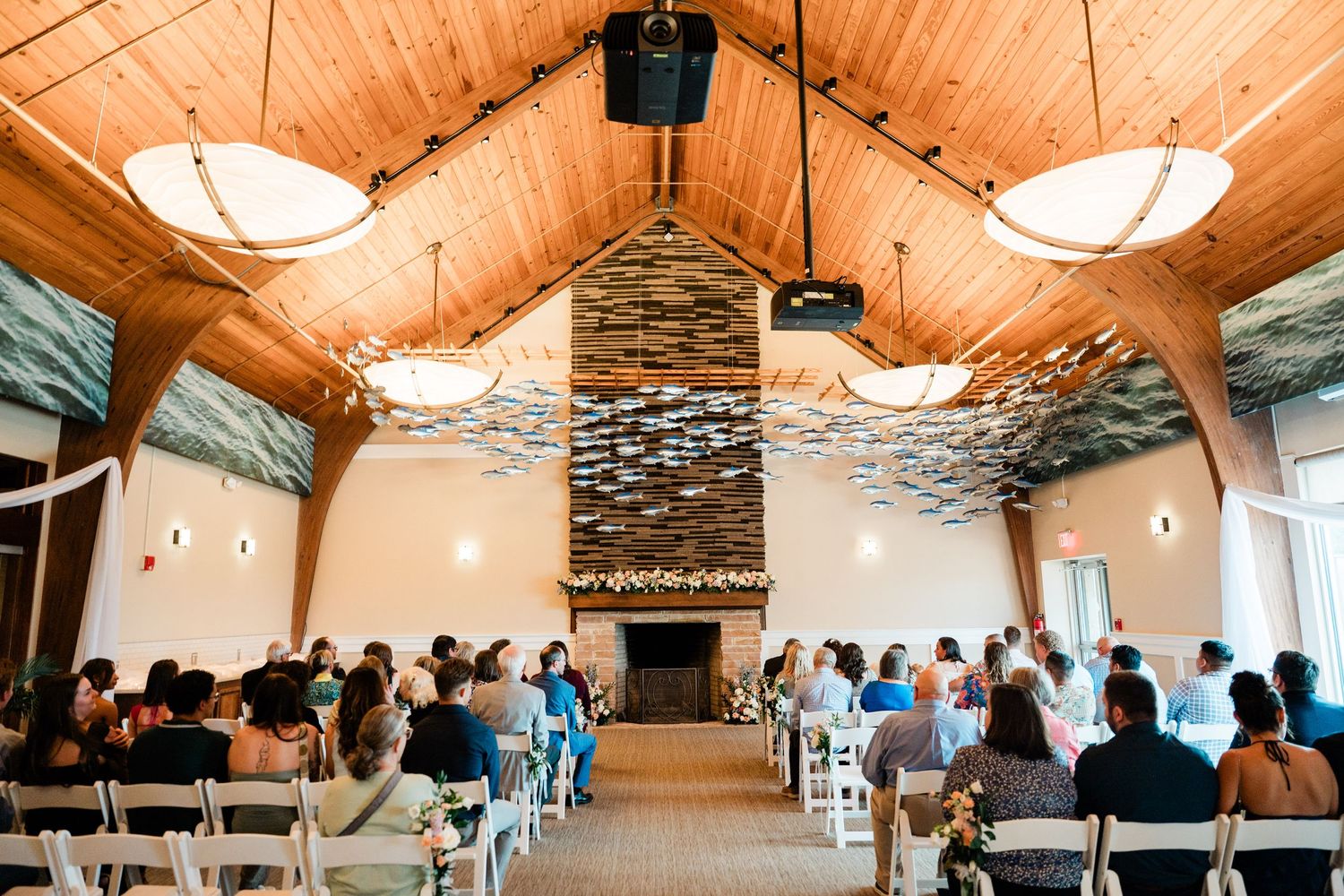Modern rustic wedding venue interior with exposed wooden beams, white walls and pendant lighting fills with guests seated.