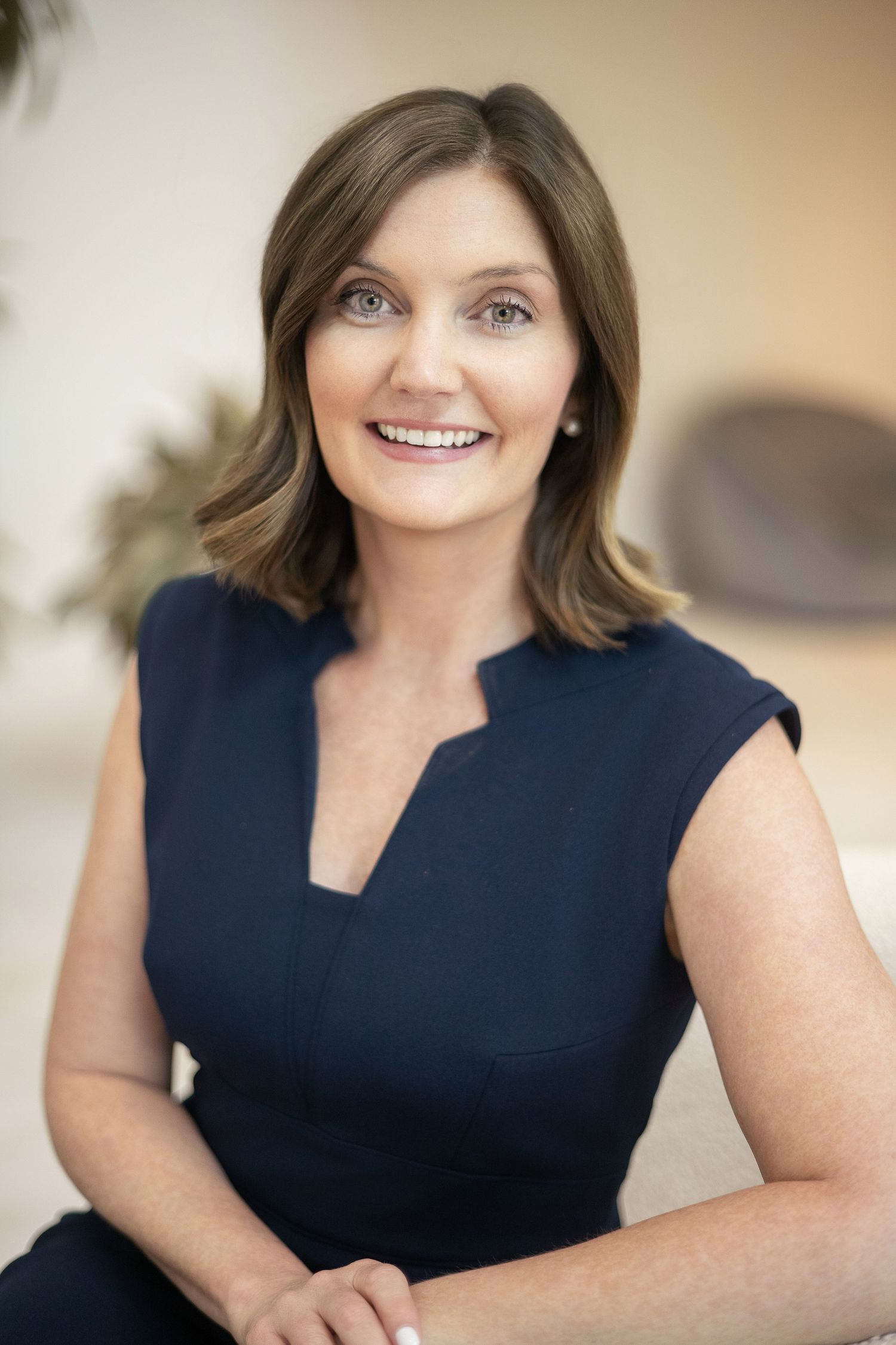 Professional woman in navy sleeveless dress smiling confidently in a bright modern office setting.