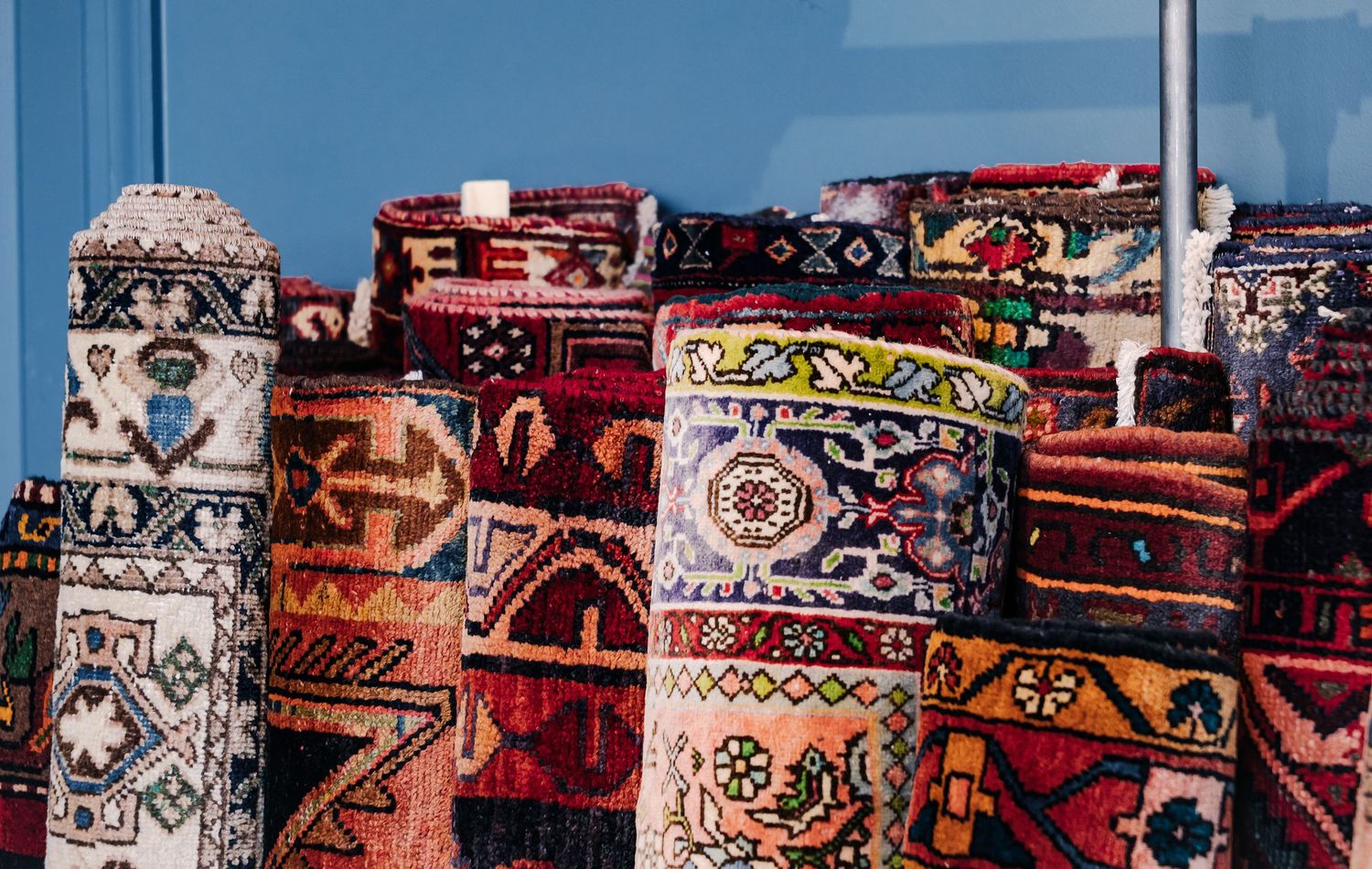 Three people smiling in a colorful rug shop surrounded by vibrant patterned rugs and eclectic home decor.