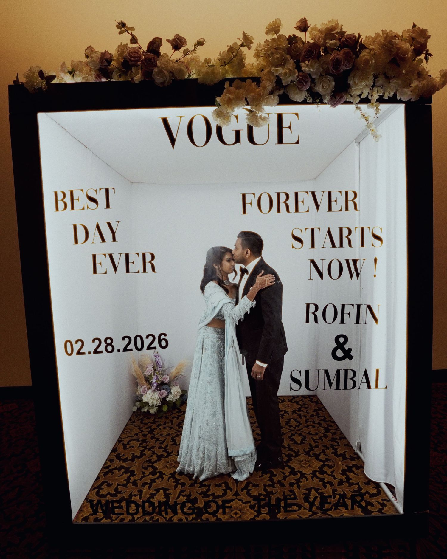 Couple kissing in a Vogue-themed wedding photo booth with text reading Rofin & Sumbal Forever Starts Now, 02.28.2026.