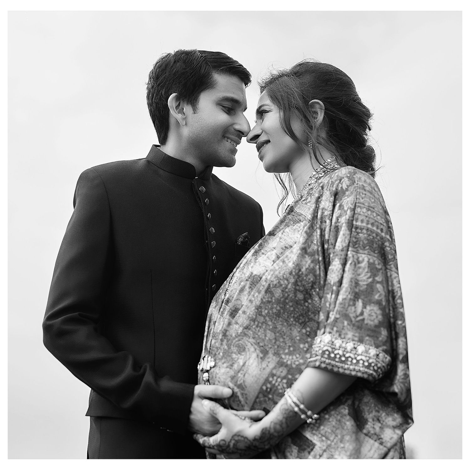 Black and white photo of a couple in traditional Indian attire sharing a romantic moment, woman appears pregnant.