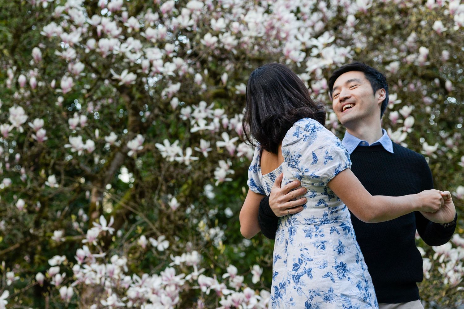 A happy couple dances and embraces in front of a lush white magnolia blossom garden.