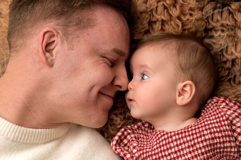 Father and baby lying face to face on a soft surface, sharing a tender moment of bonding and love.
