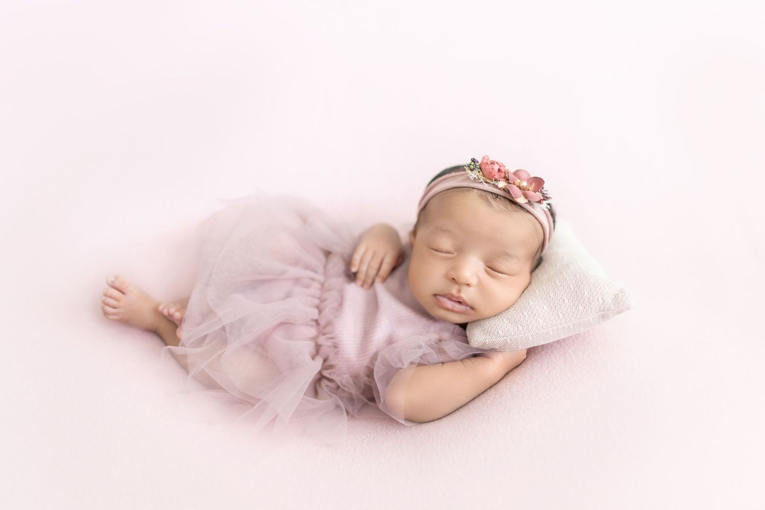 Sleeping newborn baby in soft pink dress lying on white blanket in artistic collage style photography.