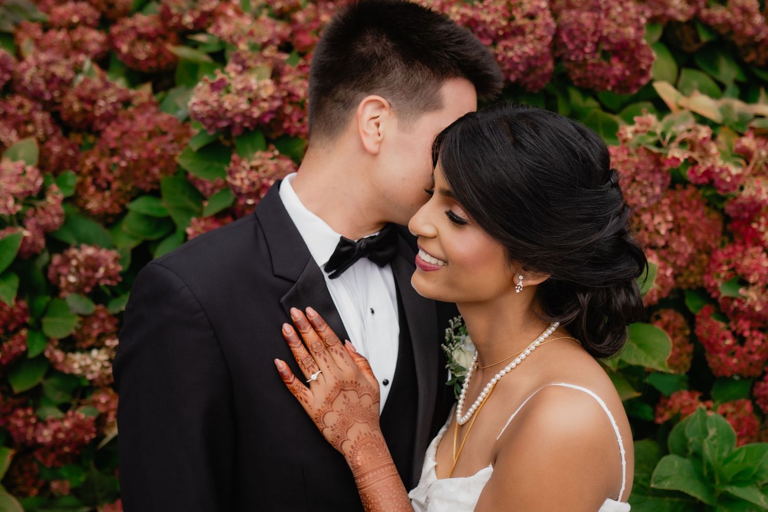 A romantic couple shares an intimate moment in front of vibrant red autumn foliage at their wedding celebration.
