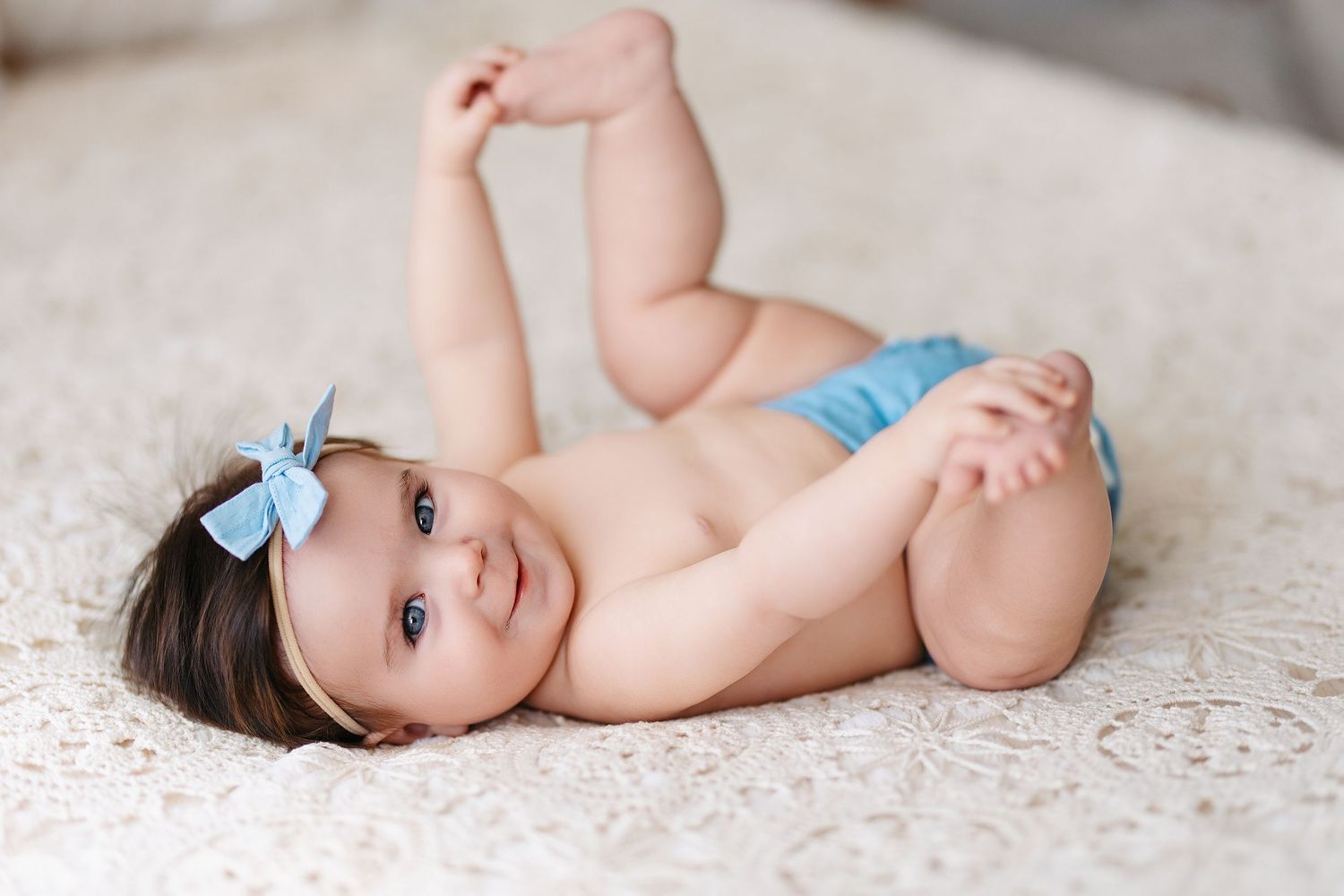 Baby in a floral dress sits on a white textured blanket with autumn decorations around them.