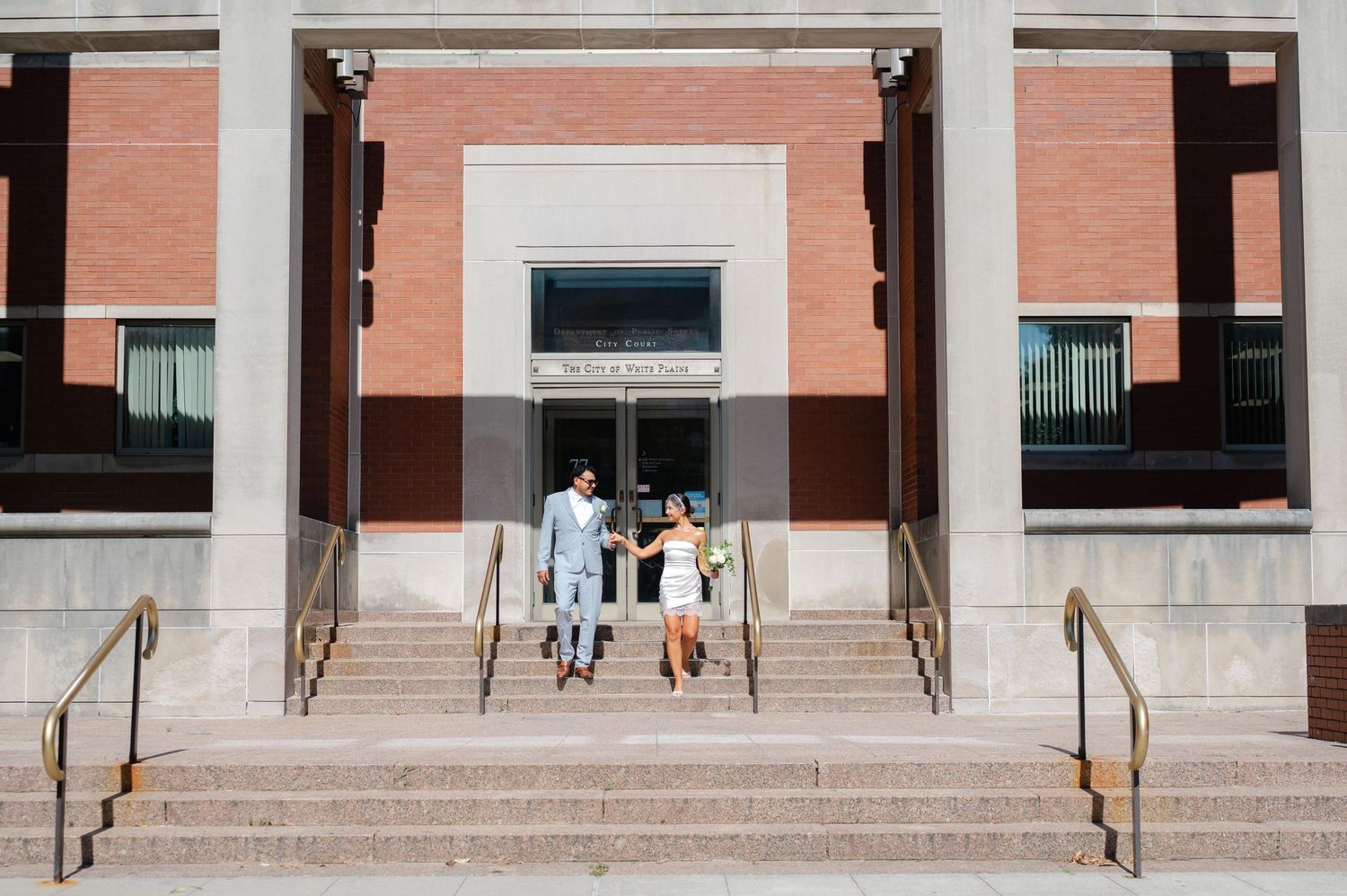 A newlywed couple walks down the steps of White Plains Courthouse after eloping in Westchester County, NY.