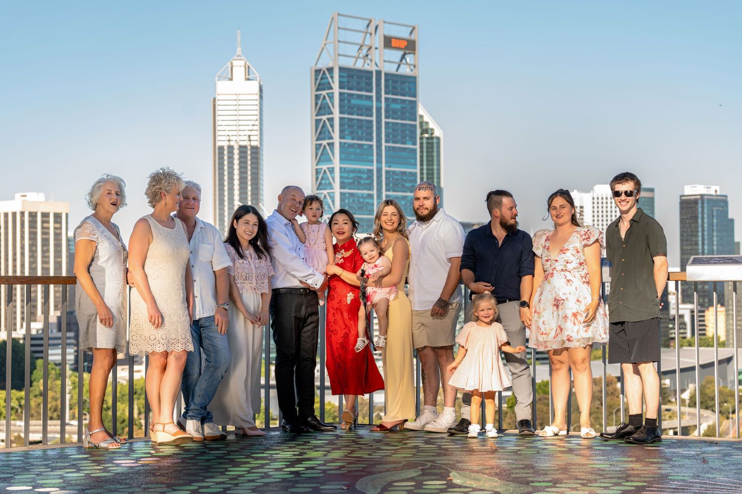 Group of people standing in a row on a beach with high-rise buildings visible in the background during sunset.