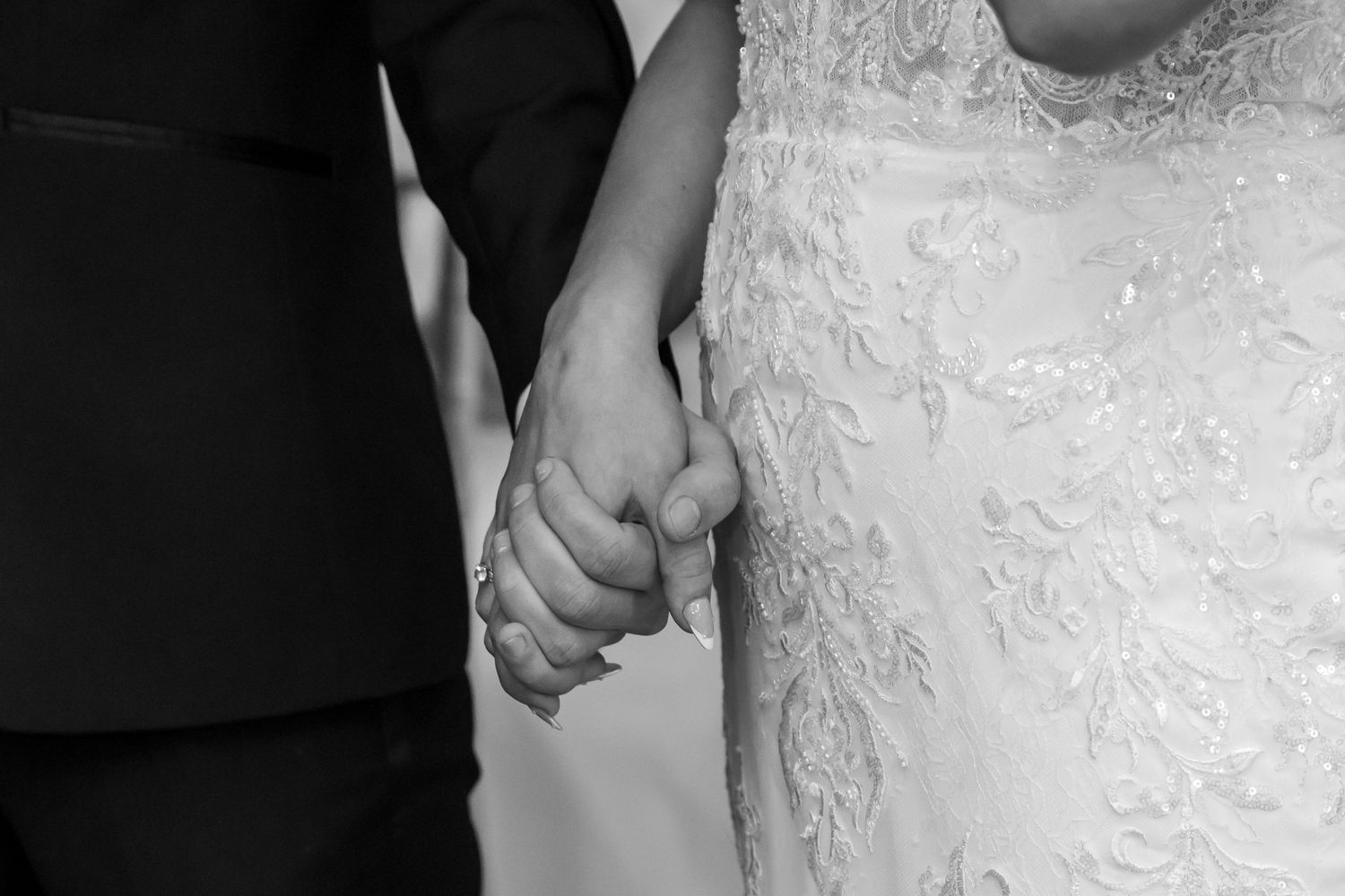 Black and white photo of a bride and groom holding hands, showcasing wedding attire at their ceremony.