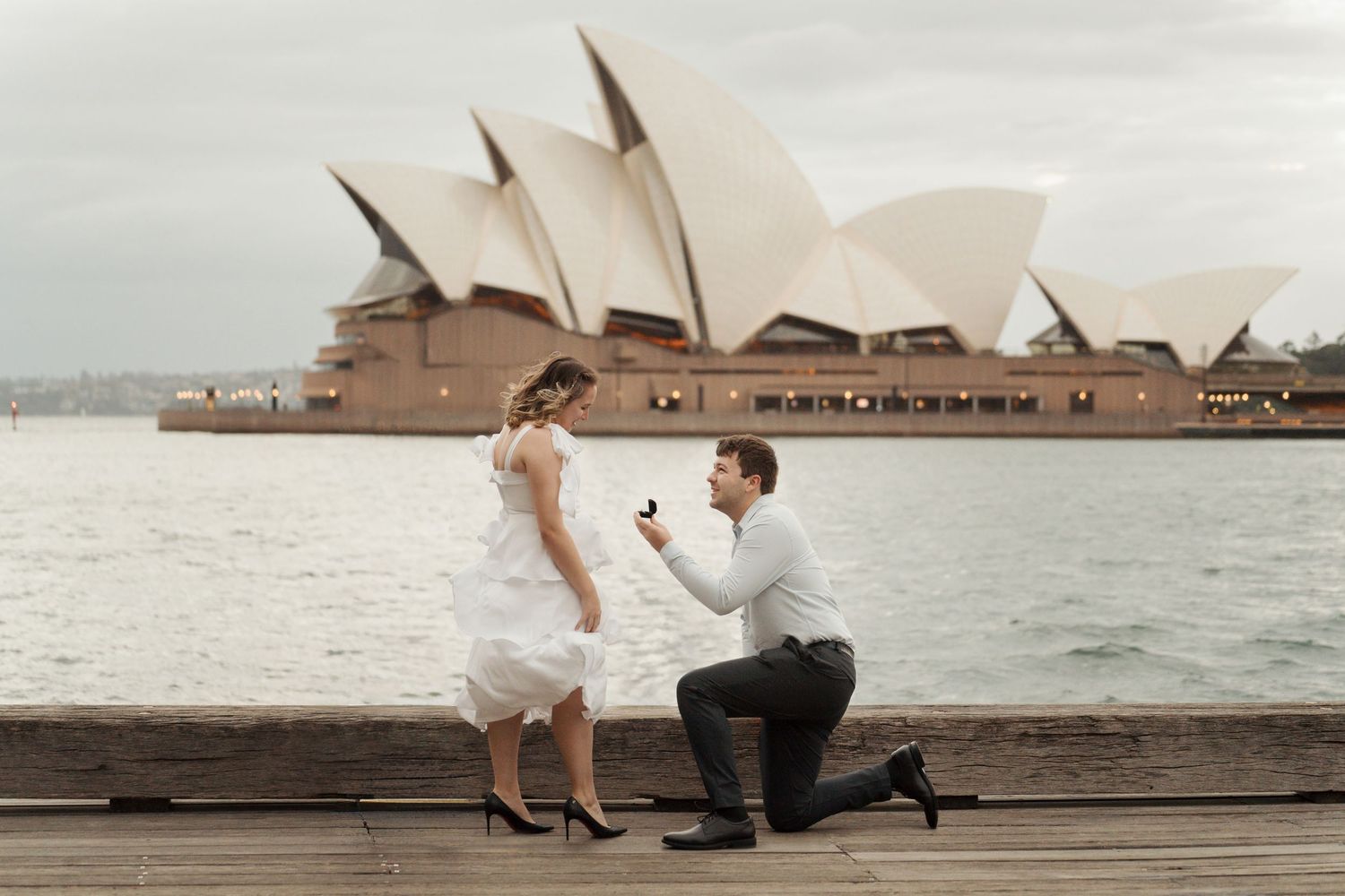 A romantic proposal moment with the iconic Sydney Opera House in the background along the harbour during a surprise proposal photoshoot i