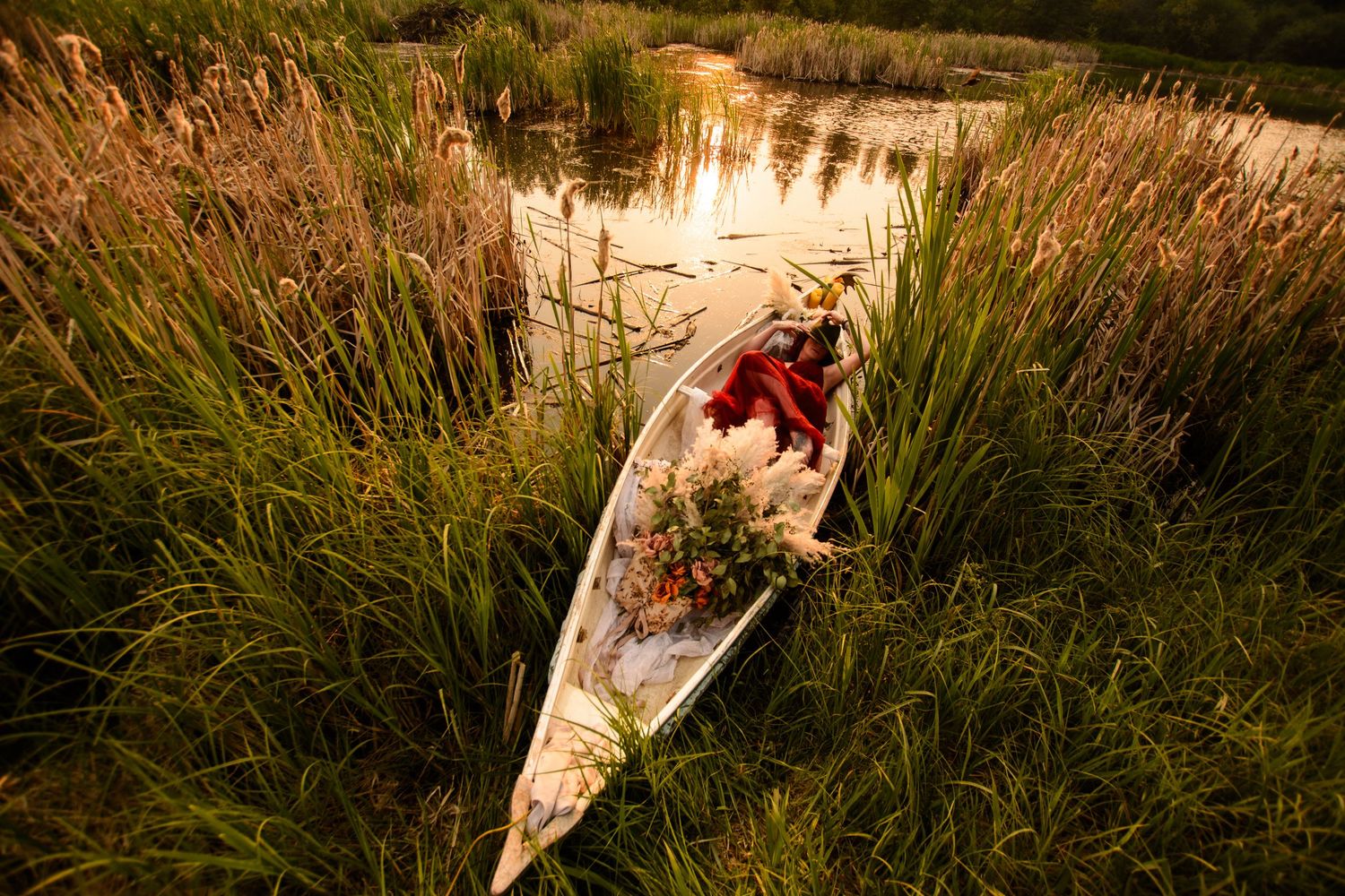 A couple in elegant white attire poses together in a golden field of tall grass at sunset.