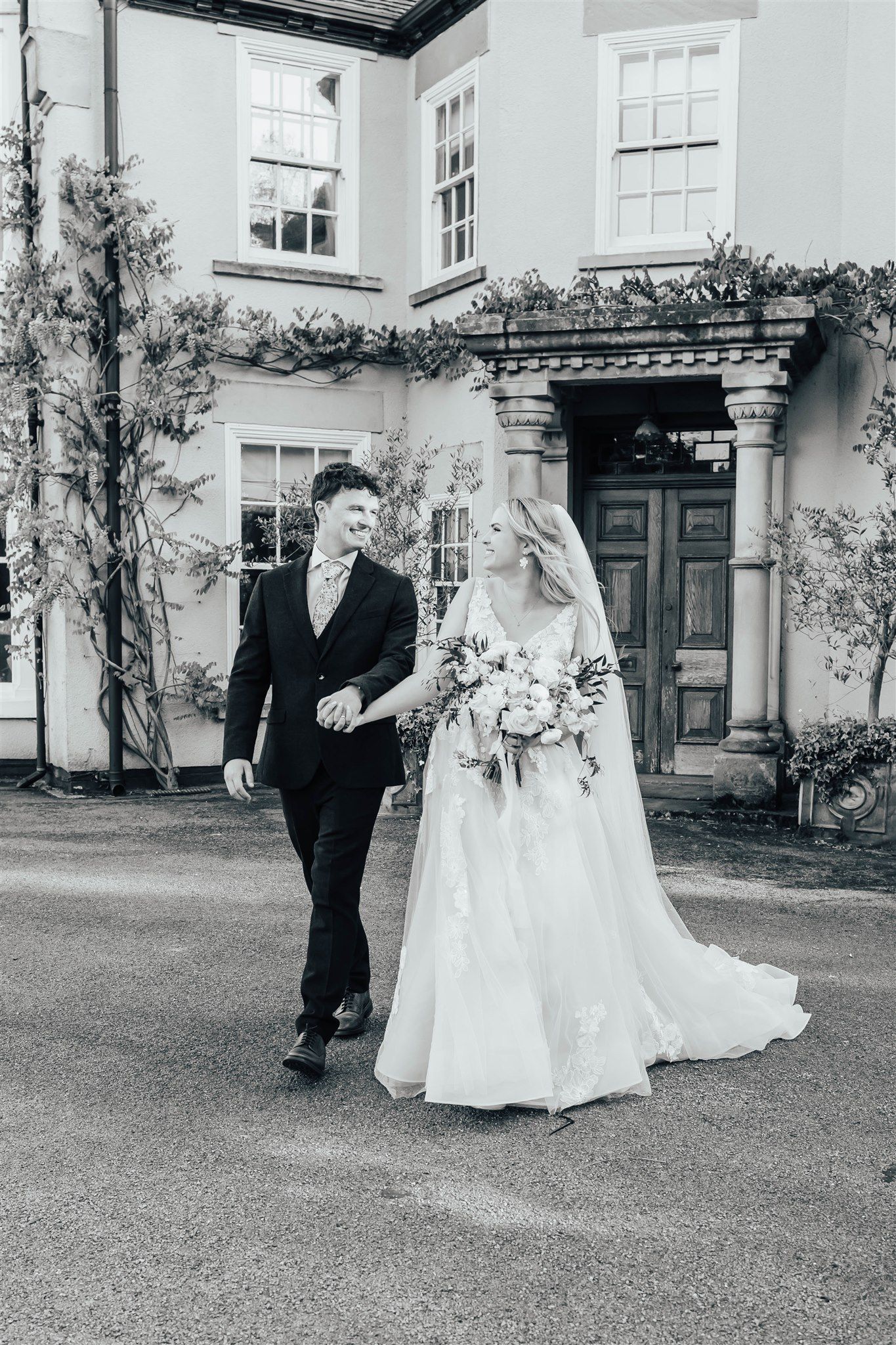 Black and white wedding photo series showing a couple walking in a garden sequence outside a stately building.