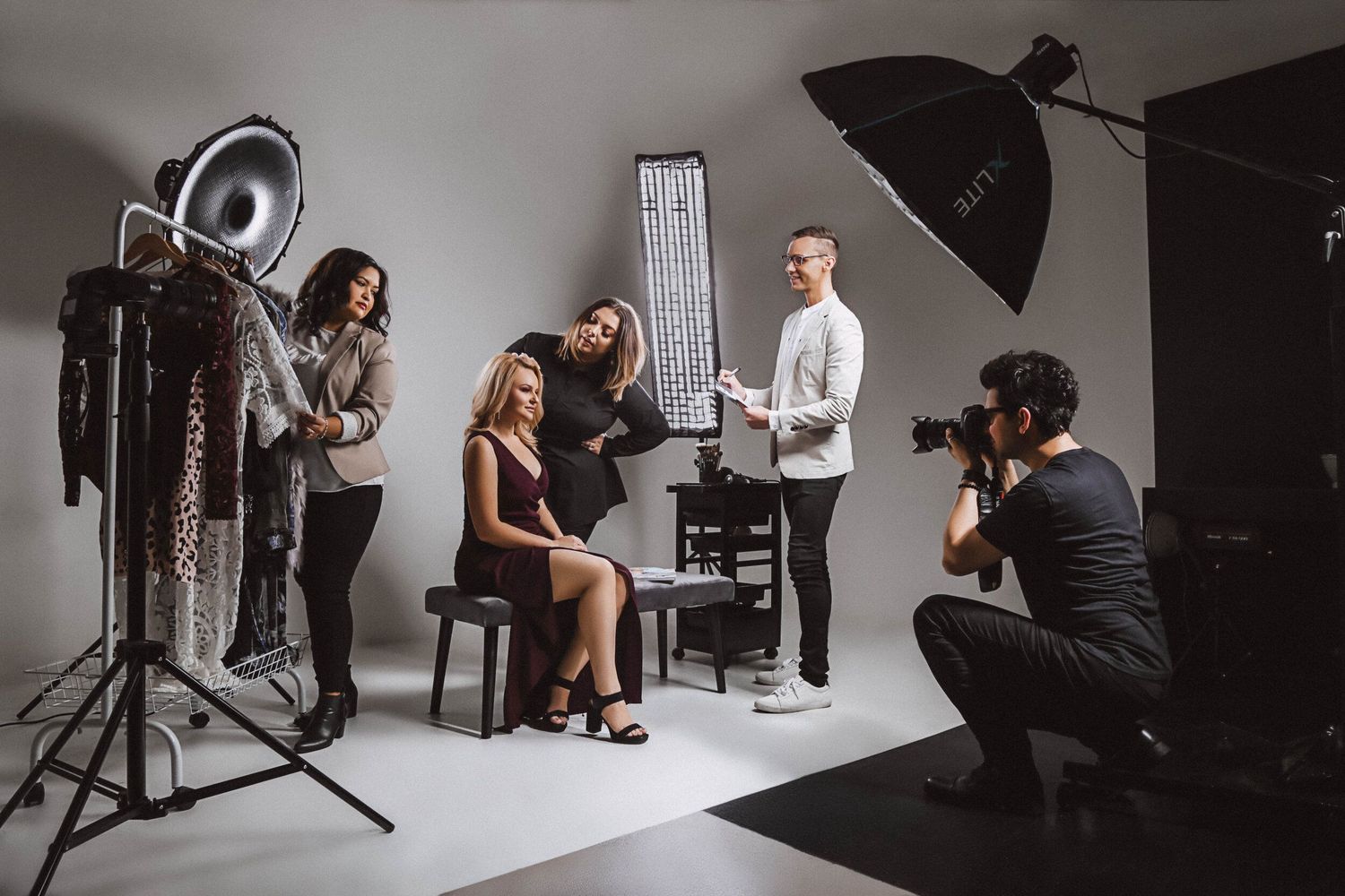 Professional photographer working with models and assistants in studio setting with lighting equipment and softboxes.