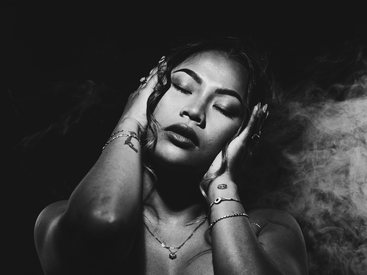 Black and white portrait of a woman with hands on her face surrounded by smoke.