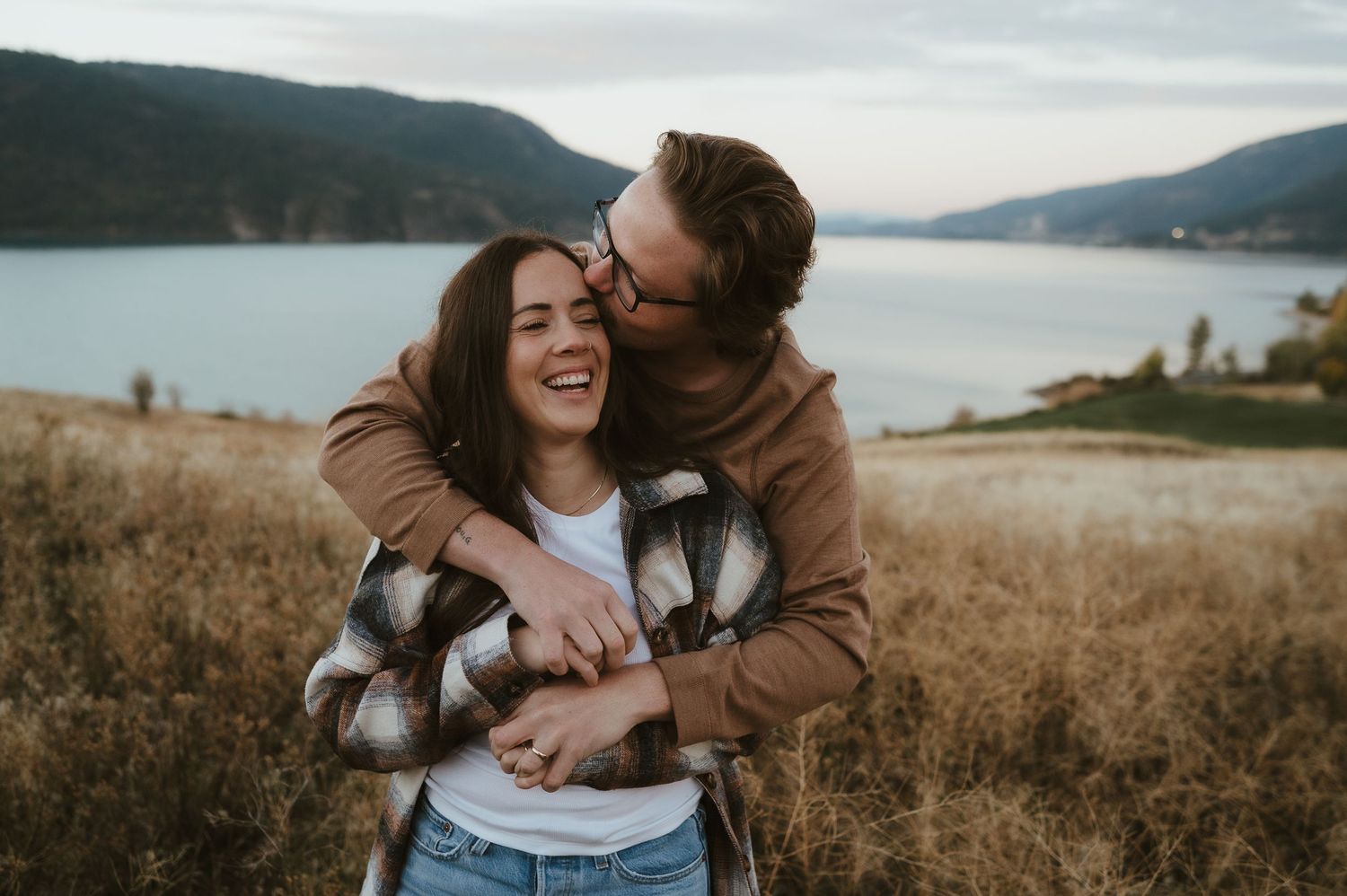 Joyful embrace in golden mountain meadow at sunset with lake vista.