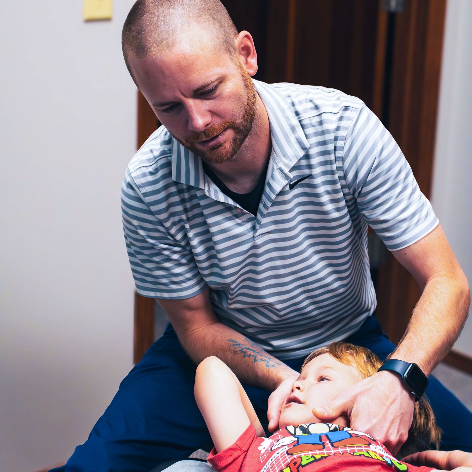 Chiropractor performs gentle adjustment on young patient in office setting.