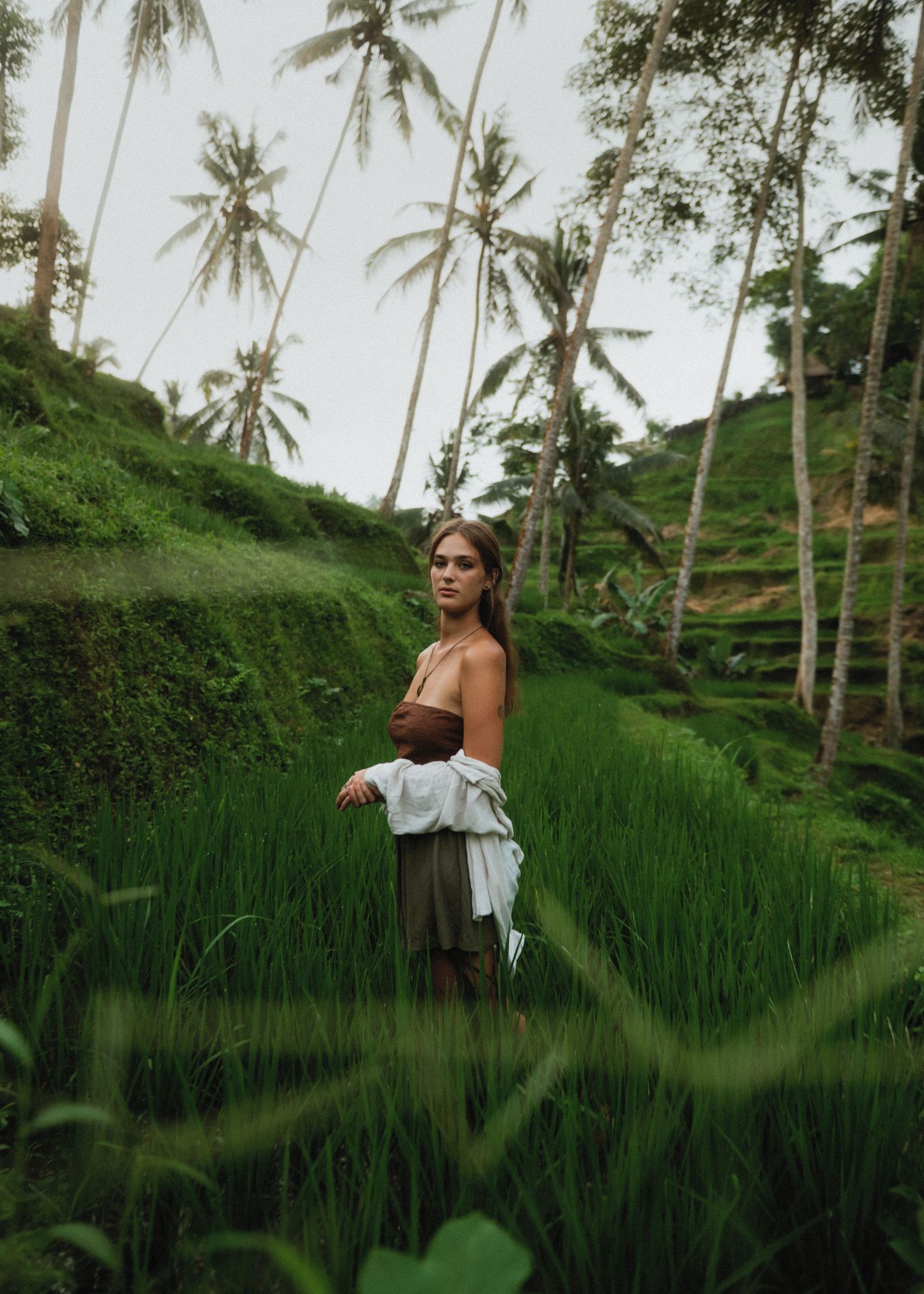 Scenic view of person in brown dress standing among lush rice terraces and palm trees in tropical setting.