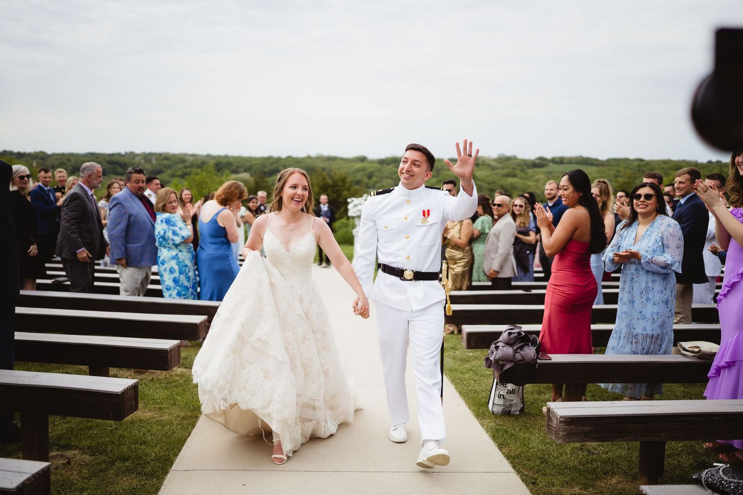 Outdoor wedding ceremony with flower arrangements in elegant white pillars against a lush green hillside backdrop.