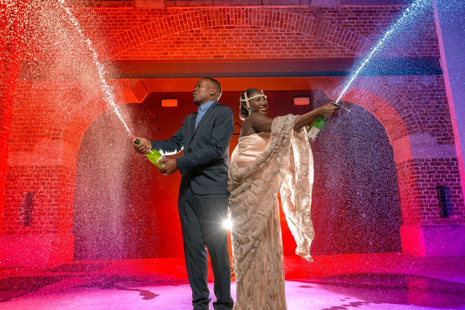 A couple in formal attire celebrating under colorful lights and sparklers in a party venue.