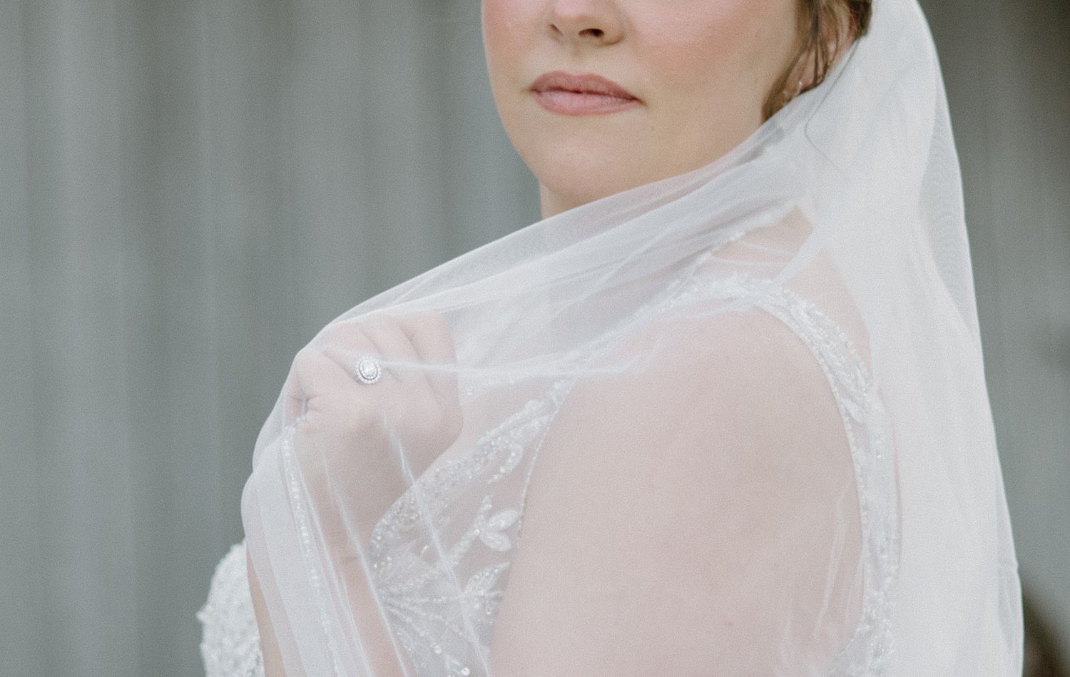 A flowing white wedding dress with long train billows in the breeze on a winter lawn surrounded by bare trees.