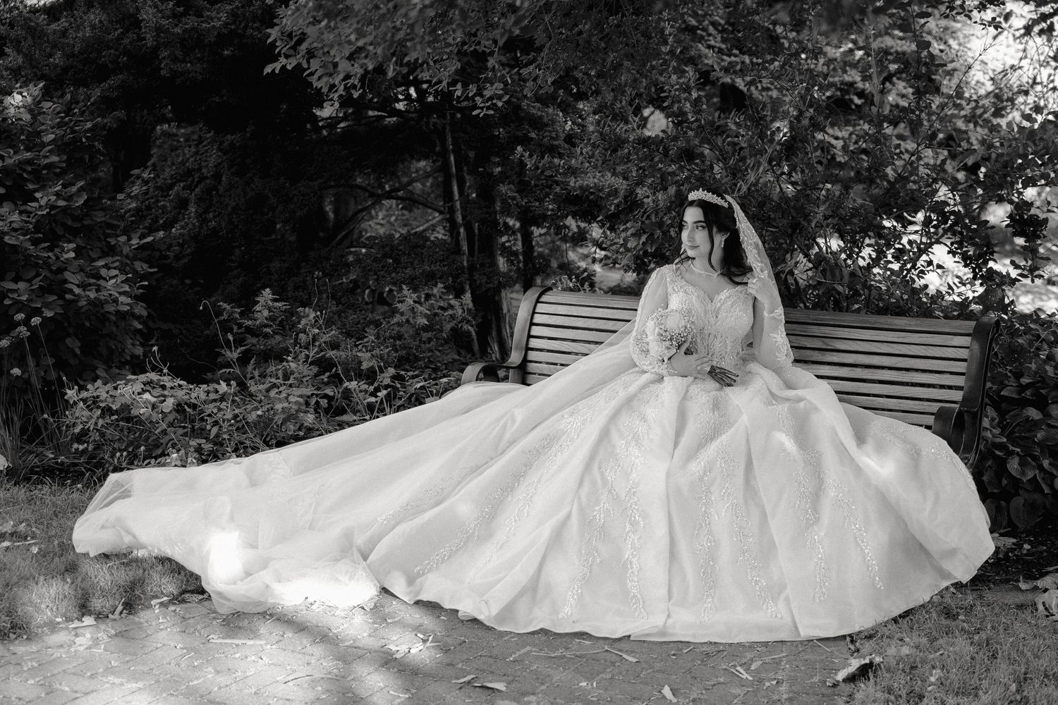 a bride sits on a bench, holding a bouquet, being photographed.