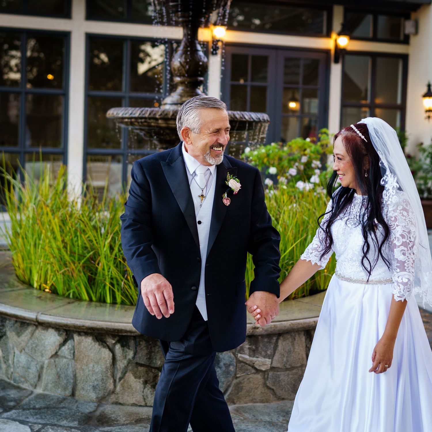 A couple in wedding attire shares a joyful moment outside near decorative lighting.