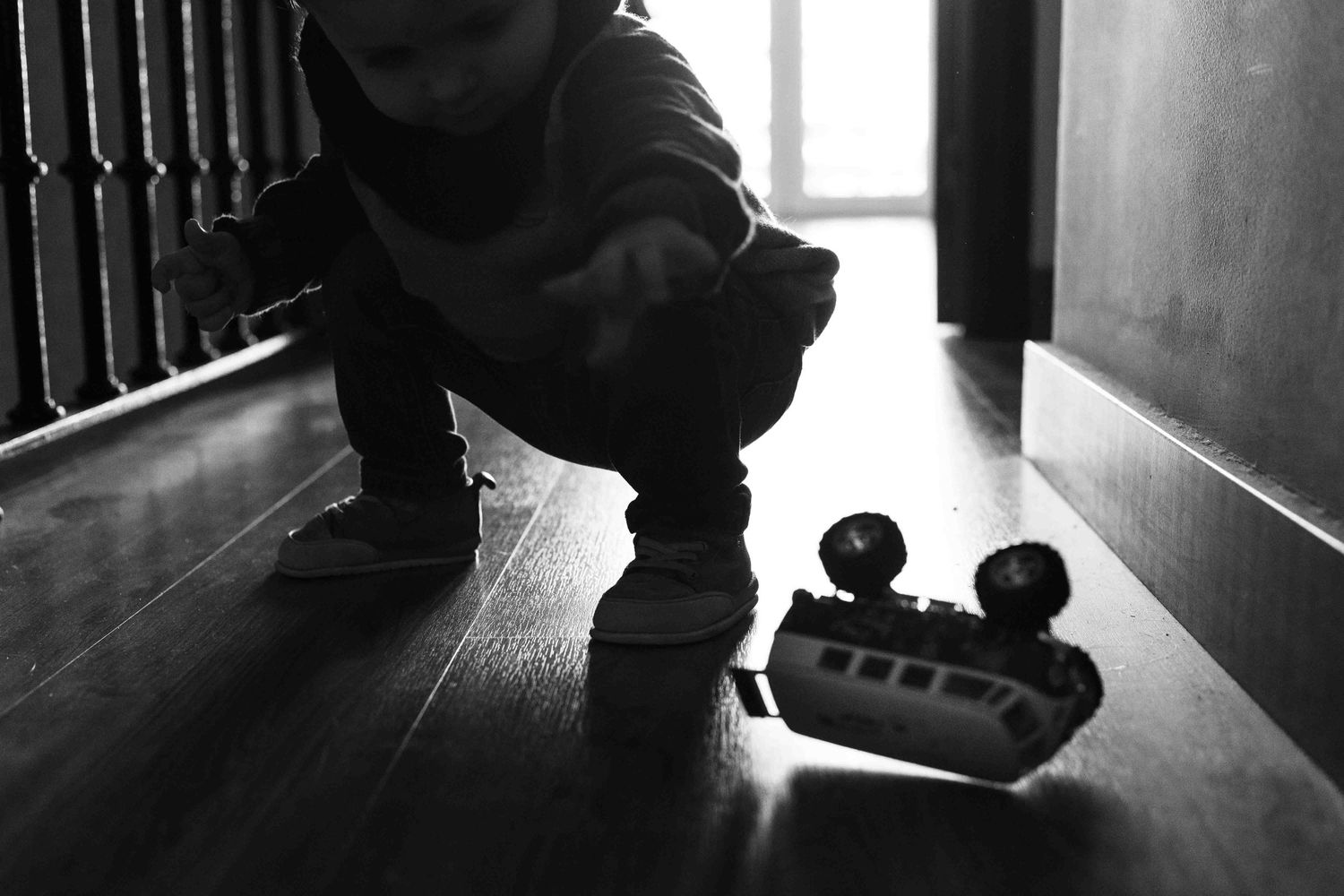 A silhouetted figure crouches in a dark hallway near a pair of rollerblades or small wheels on the wooden floor.