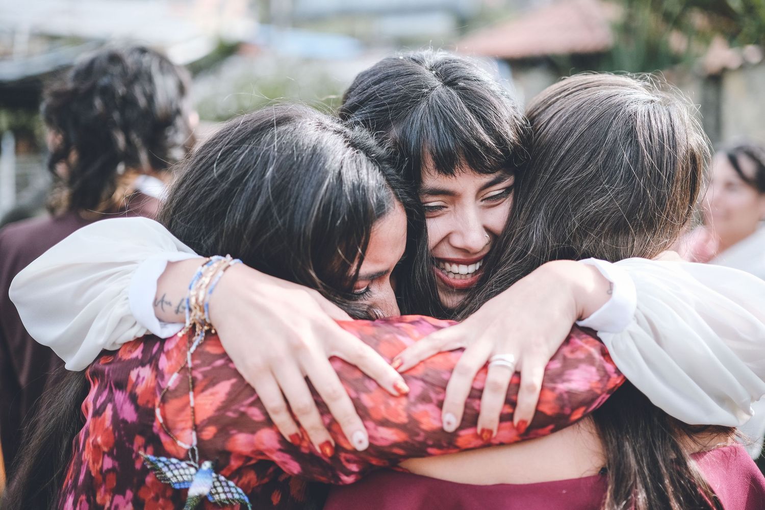 Three friends share a warm group hug while wearing flowing white sleeves.