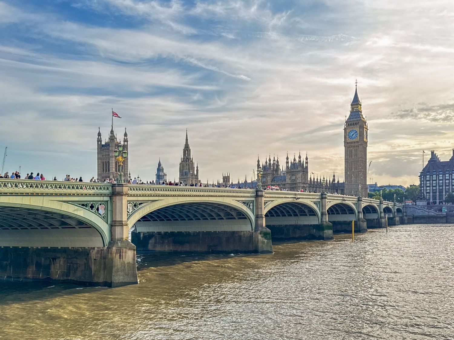 A panoramic view of the iconic London skyline with Big Ben and Westminster Bridge reflected in the River Thames on a bright day.