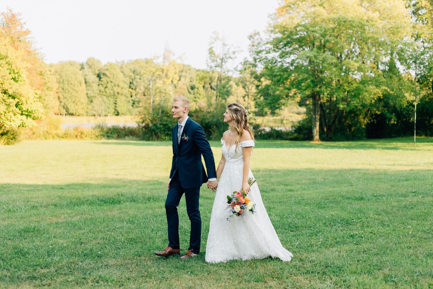 A couple shares a tender moment during their outdoor autumn wedding on a sunlit grassy field.
