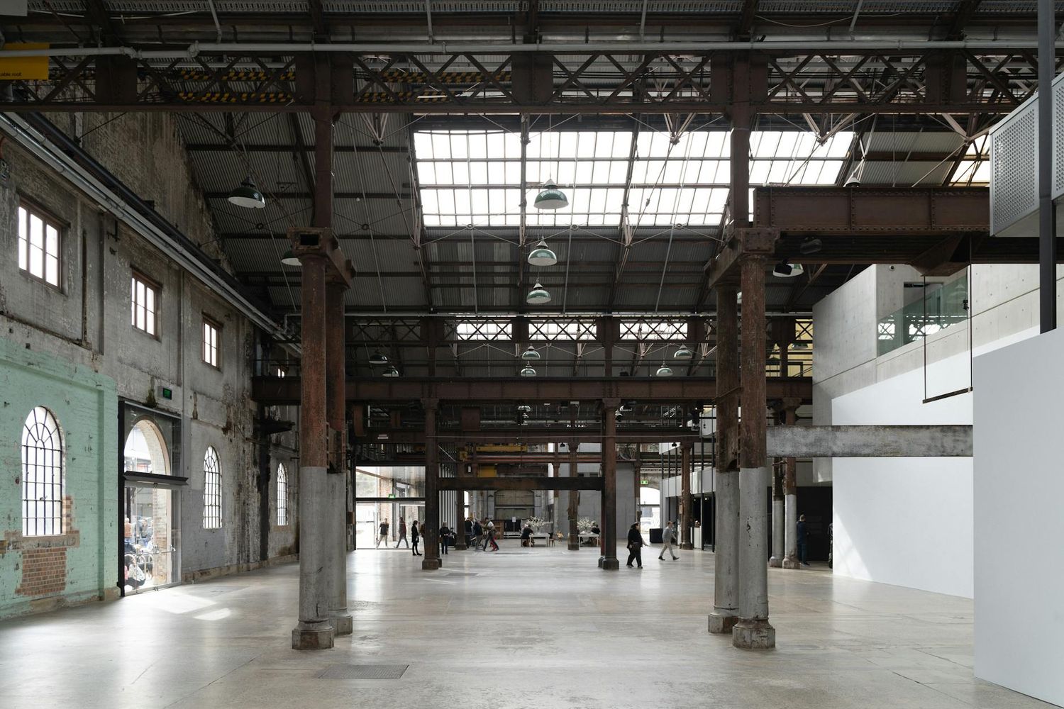 Interior of an industrial warehouse space with exposed columns, high ceilings and natural light streaming through windows.