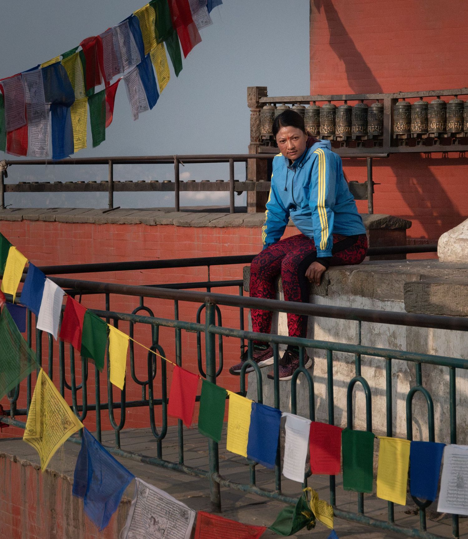 Traditional prayer flags wave over a stairway in Nepal with red brick walls in the background.