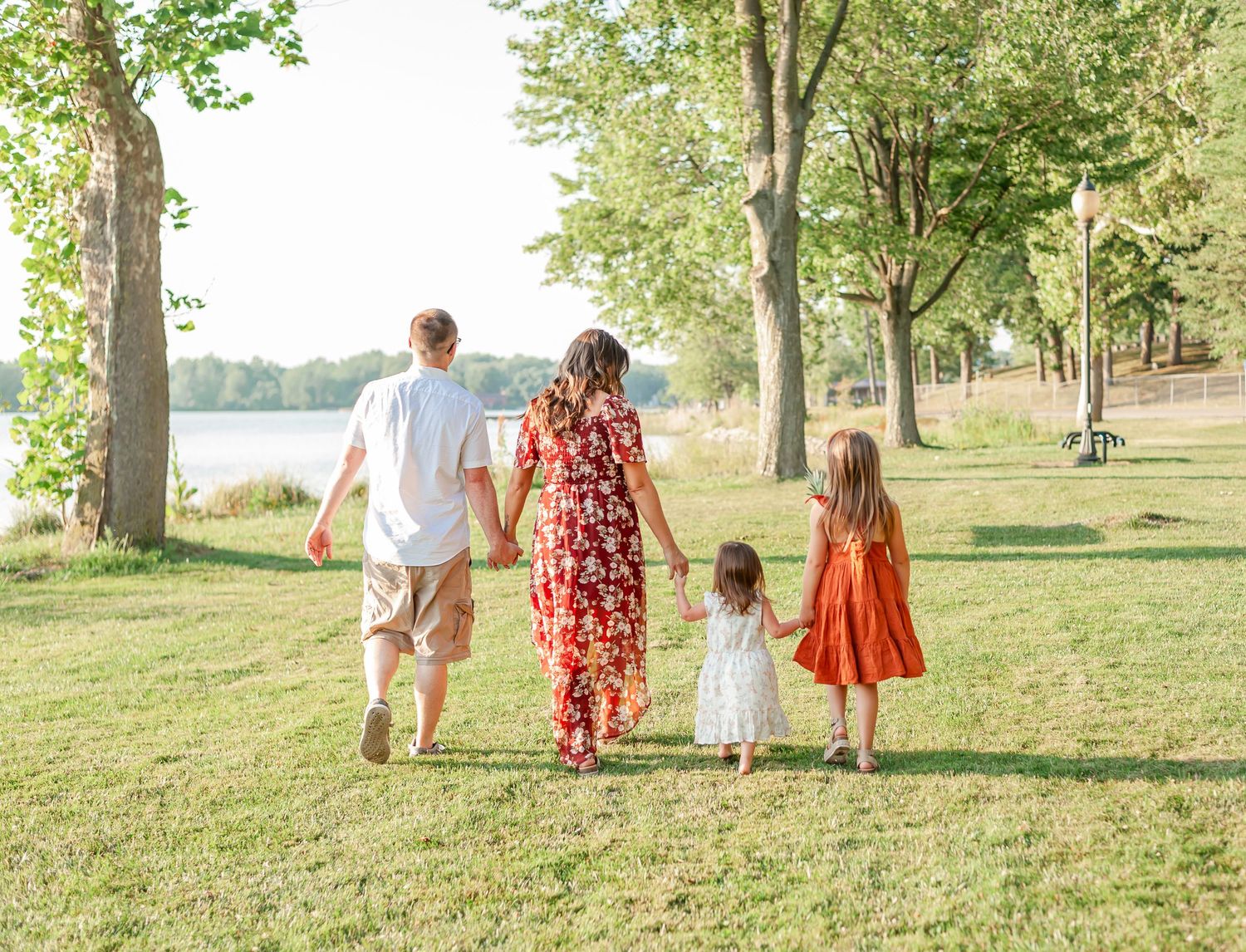 A family walks together on a grassy path near a lake during a summer evening.