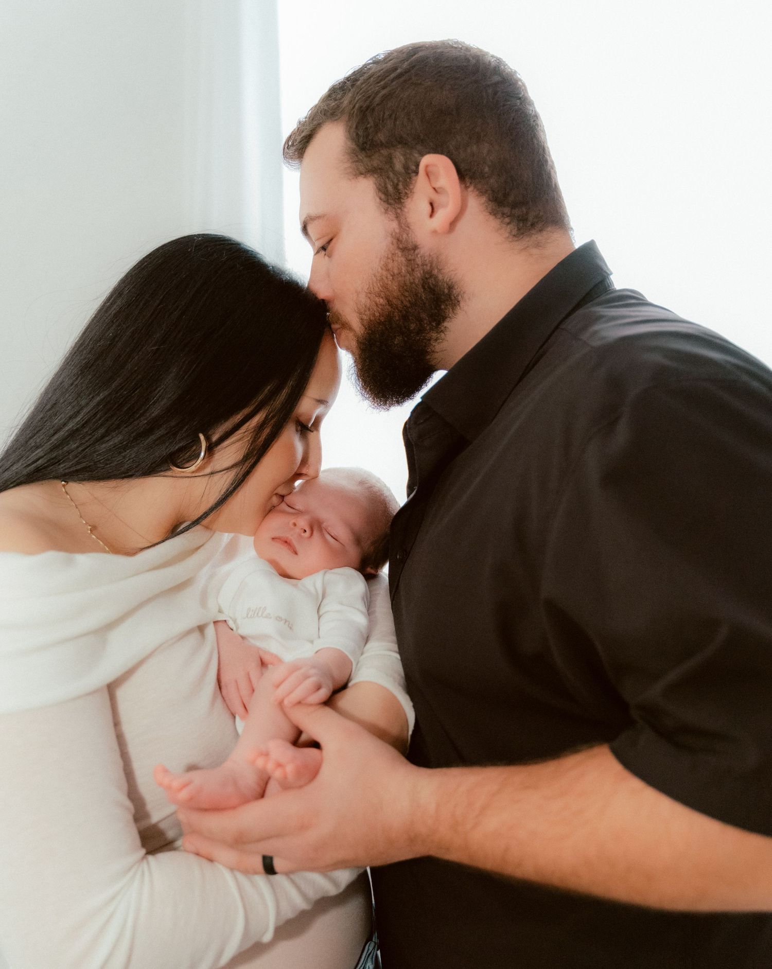 Intimate family moment sharing tender embrace with newborn baby in white.