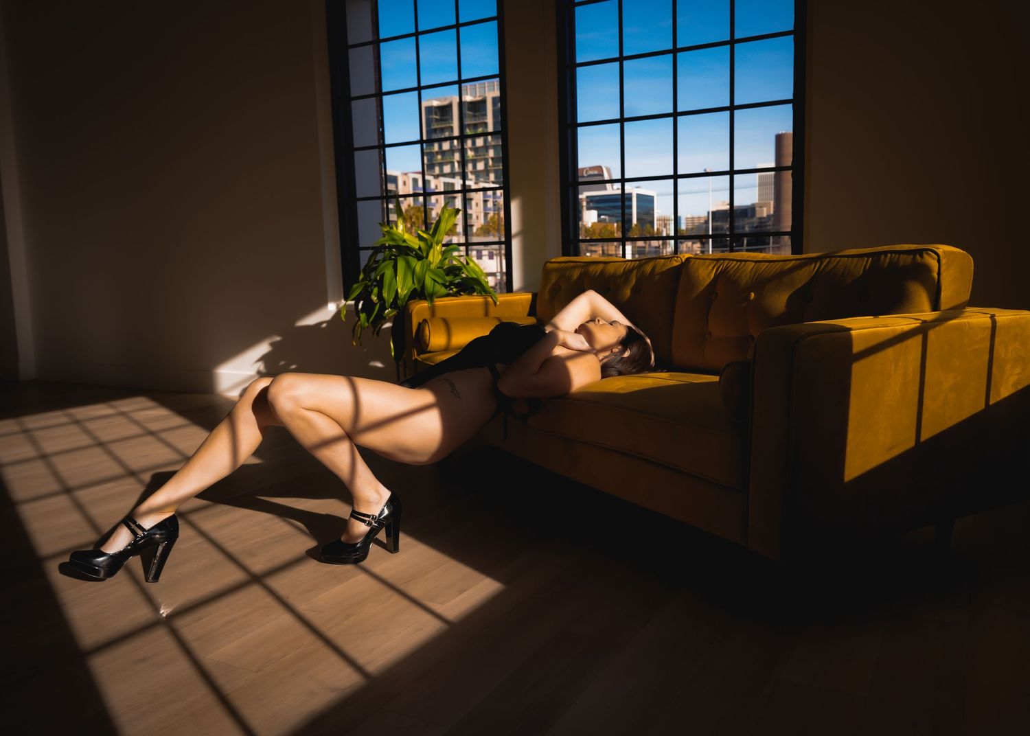 Dramatic sunlight streams through gridded windows onto a modern living room with yellow decor and a decorative birdhouse.