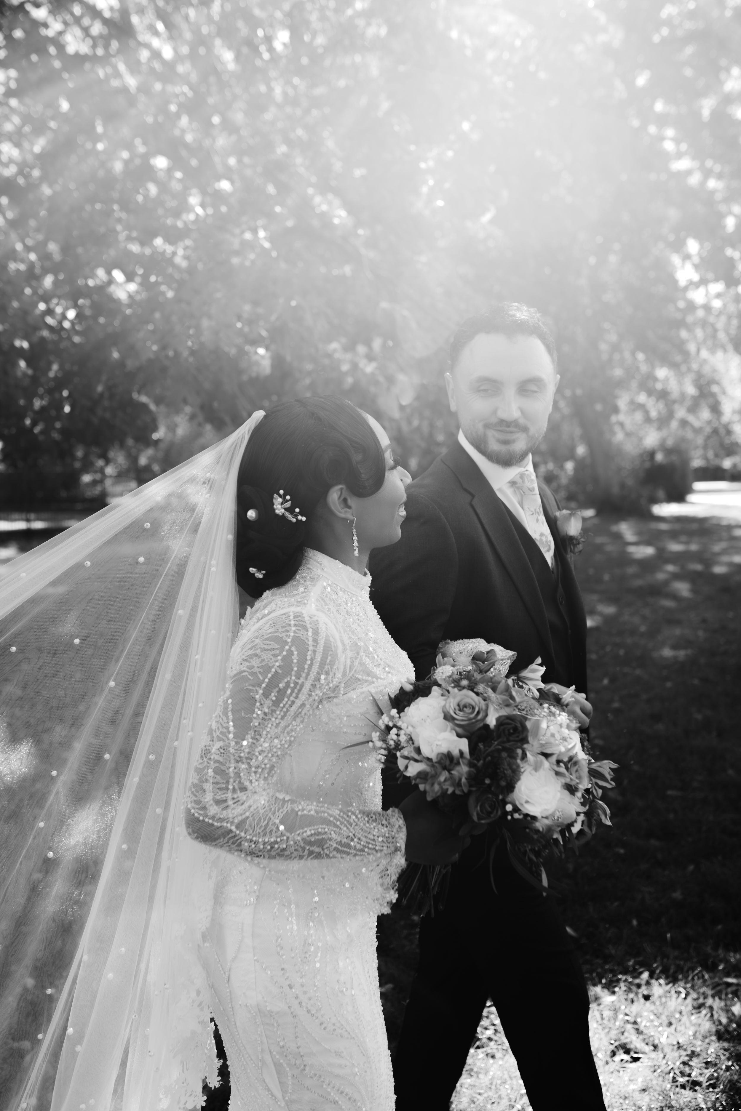 A wedding couple stands in front of an elegant ivy-covered estate entrance with arched doorway.