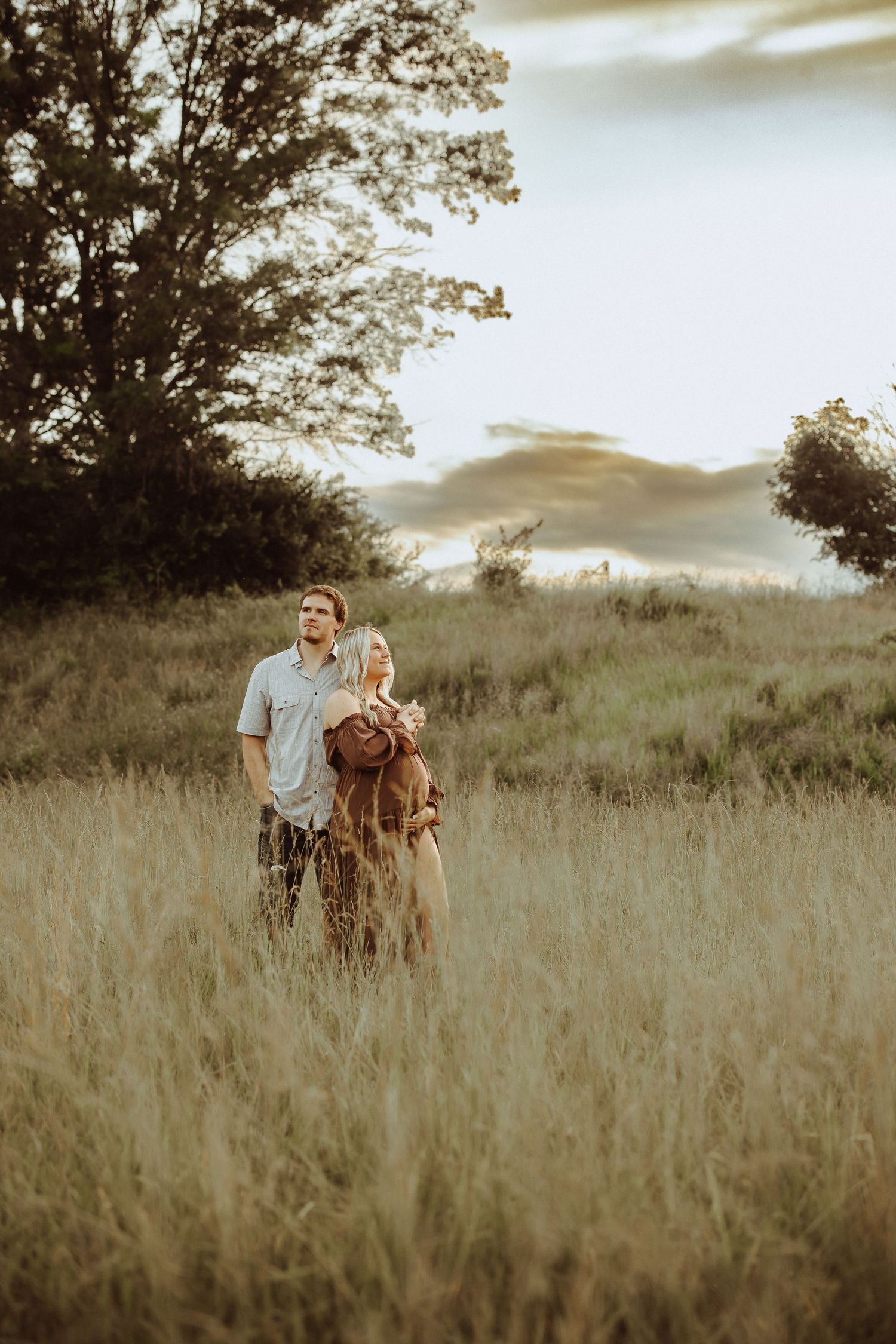 A couple stands together in a golden field during sunset for romantic photos.