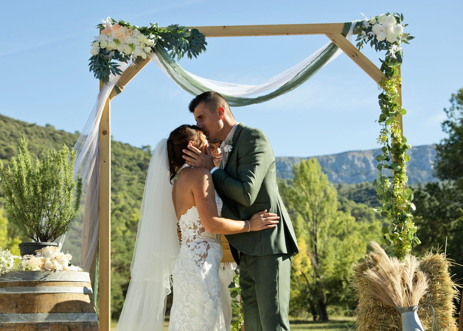 Audrey et Sébastien enlacés sous une arche fleurie lors de leur mariage à Nans-les-Pins.