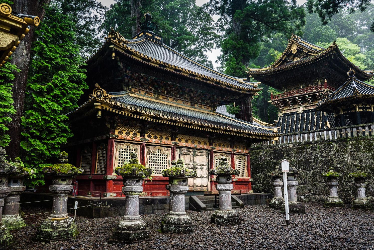 Ornate Japanese temple with gold detailing, stone lanterns, and lush green trees at Nikko Toshogu Shrine, Japan.