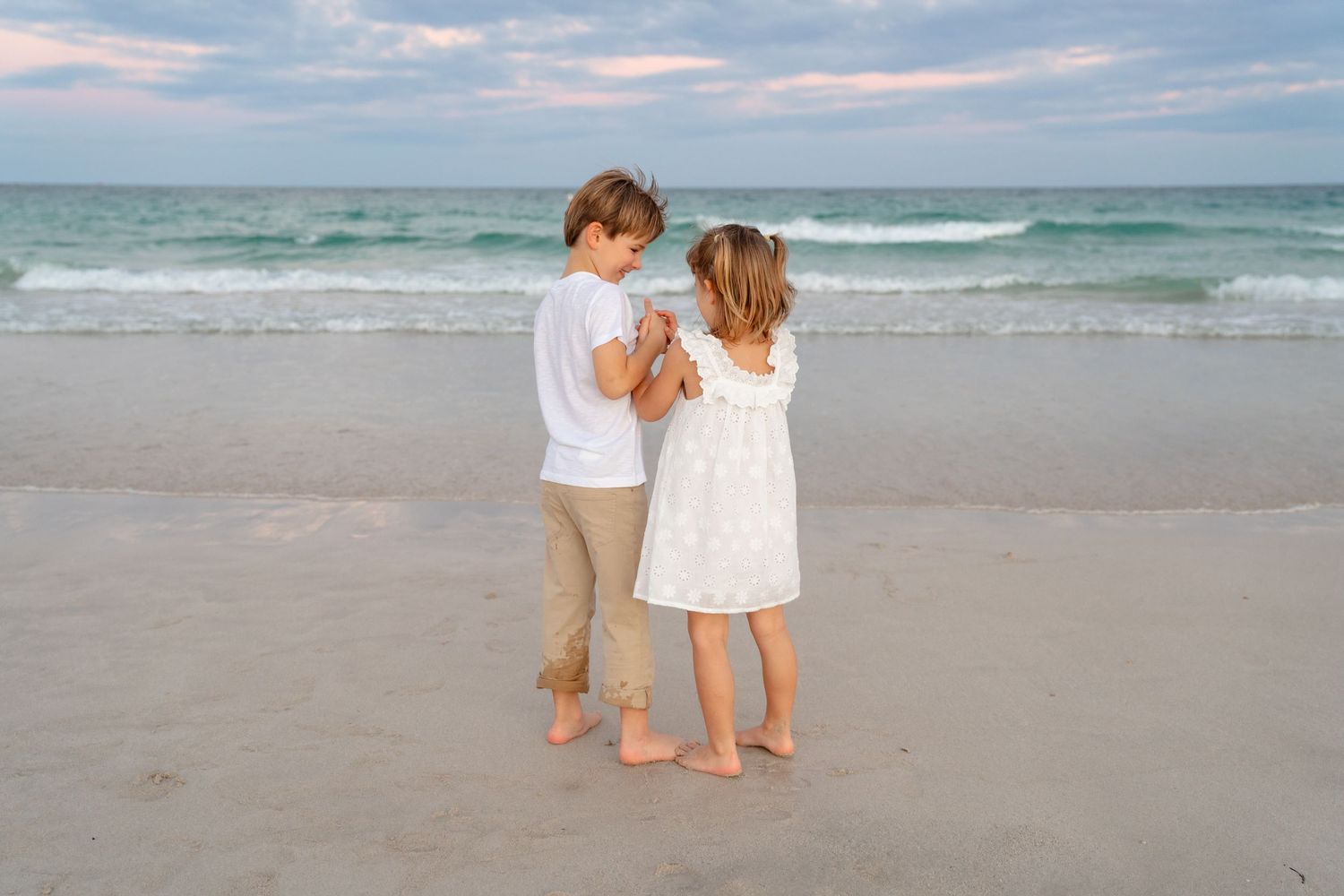 A family runs together on a sandy beach path with palm trees at sunset.