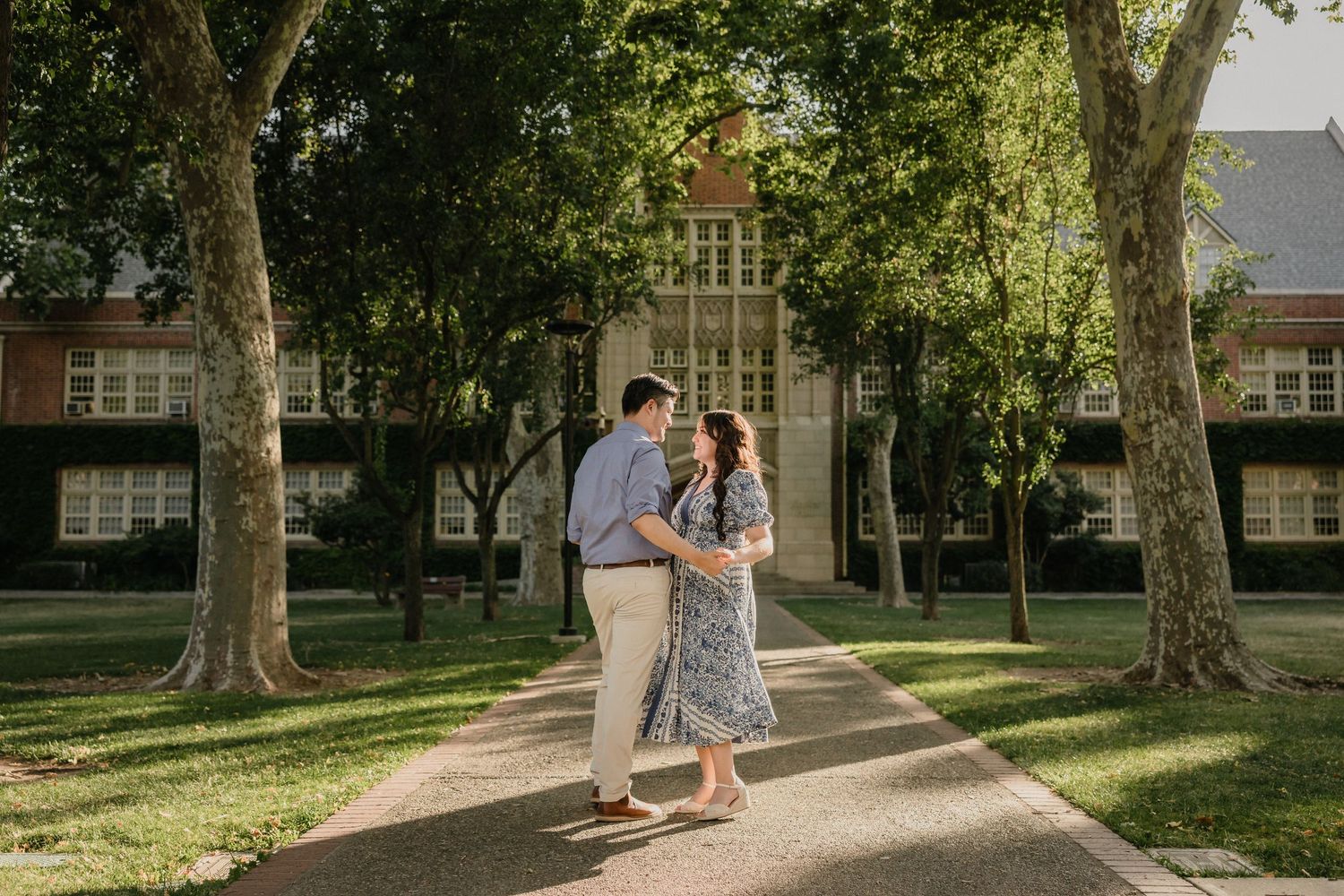 A couple walks down a tree-lined path on a sunny afternoon at a historic university campus.