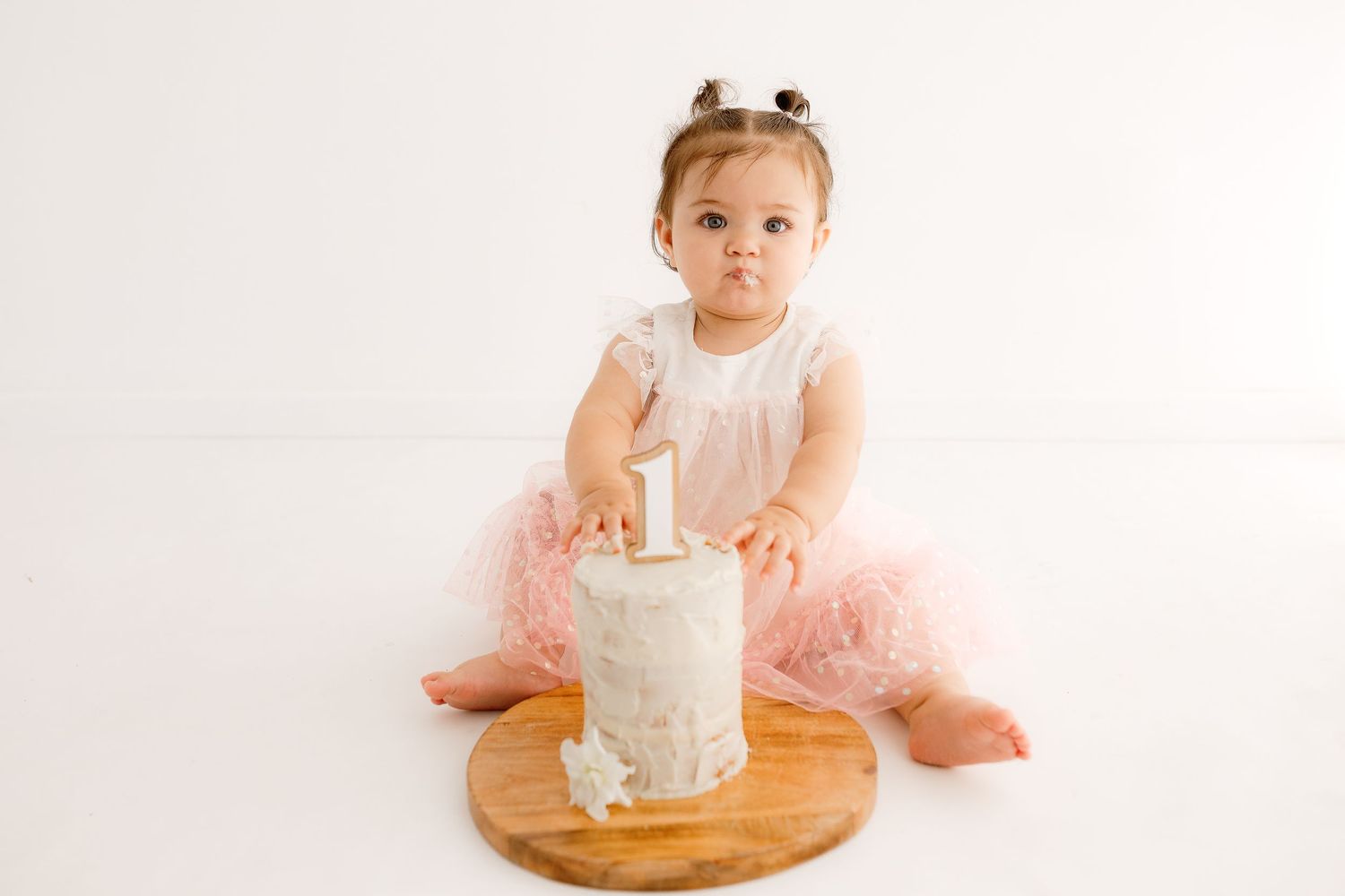 Baby in pink tutu dress sits at wooden table during first birthday photo shoot.