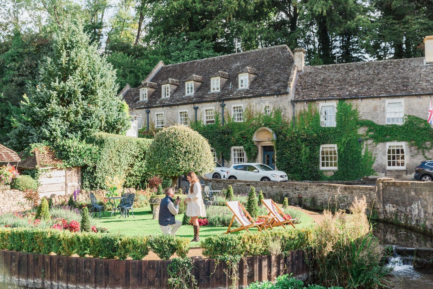 Scenic stone buildings and colorful garden chairs line a peaceful riverside setting at Bibury - Proposal Photography Hayley Elizabeth