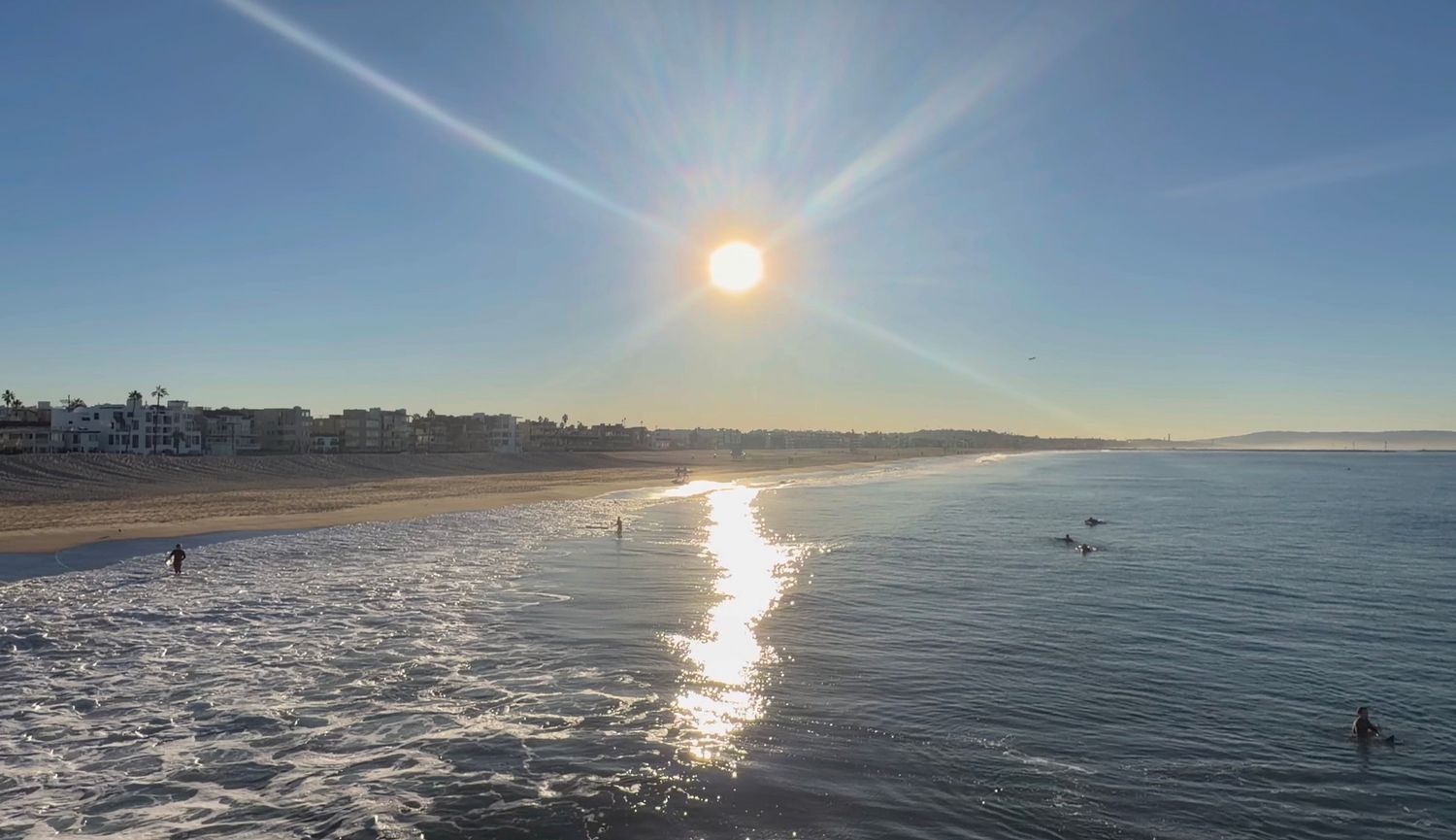 Sunlight sparkles on calm ocean waves at a scenic beach during golden hour with silhouettes in the distance.