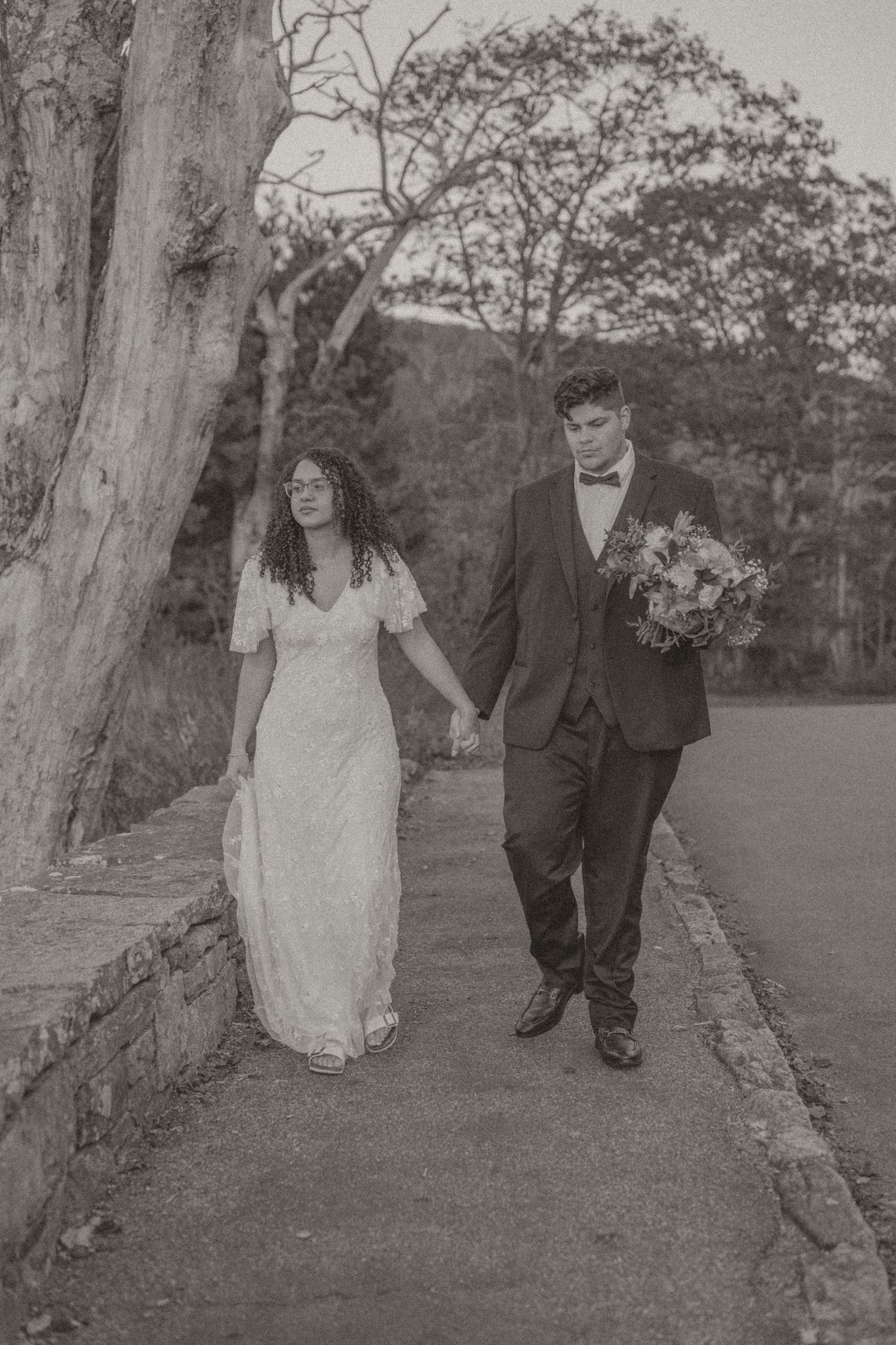 Black and white photo series showing a couple walking together on a tree-lined path in wedding attire.